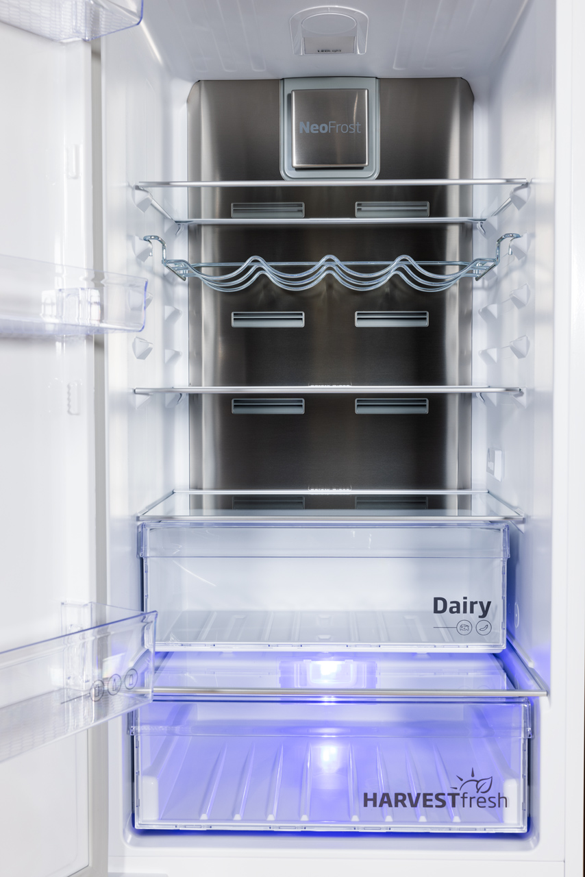 Puste wnętrze lodówki z półkami i szufladami. Zawiera sekcje nabiału i świeżych produktów.
