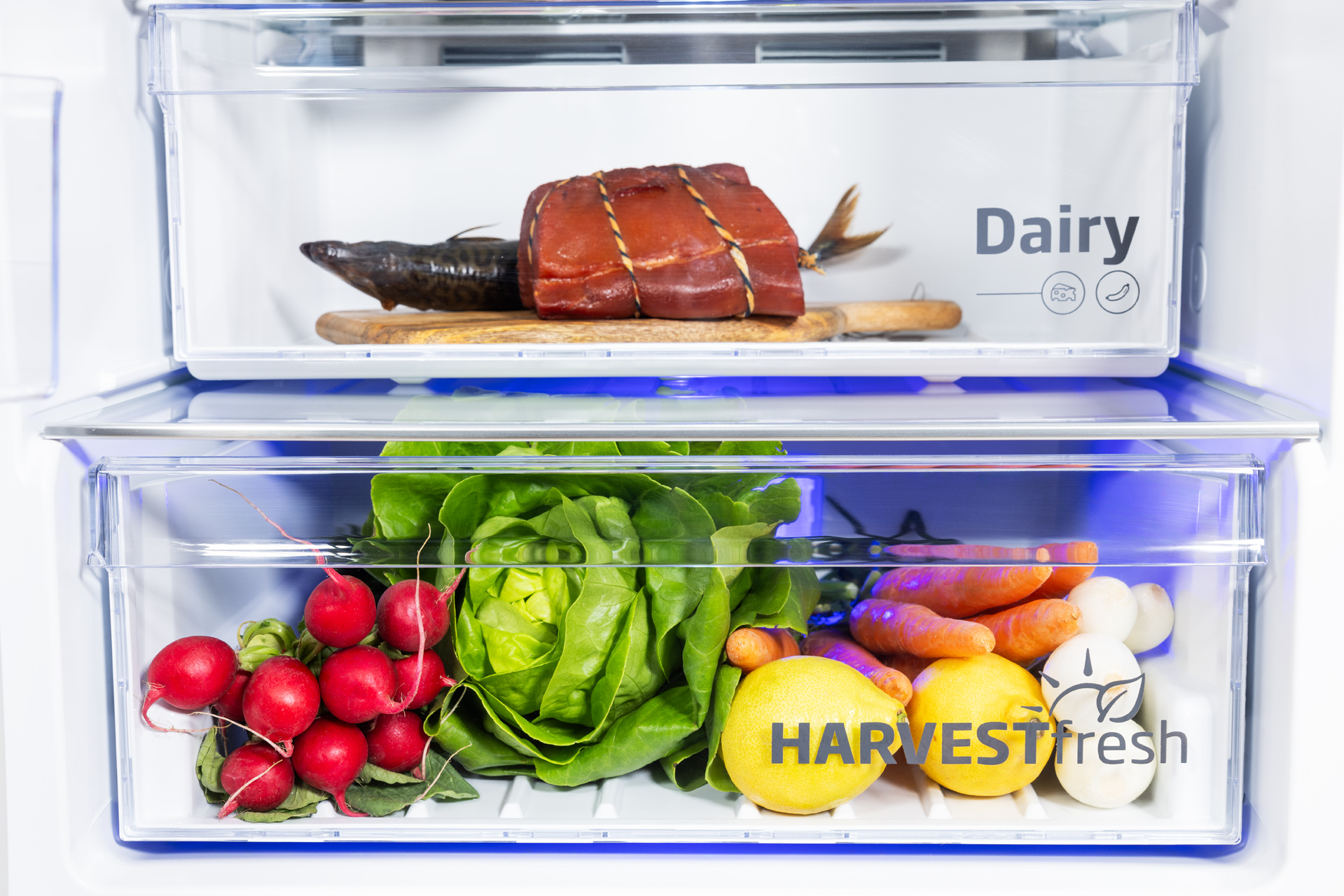 Wnętrze lodówki z dwiema szufladami z jedzeniem: nabiał na górze, warzywa i owoce na dole.