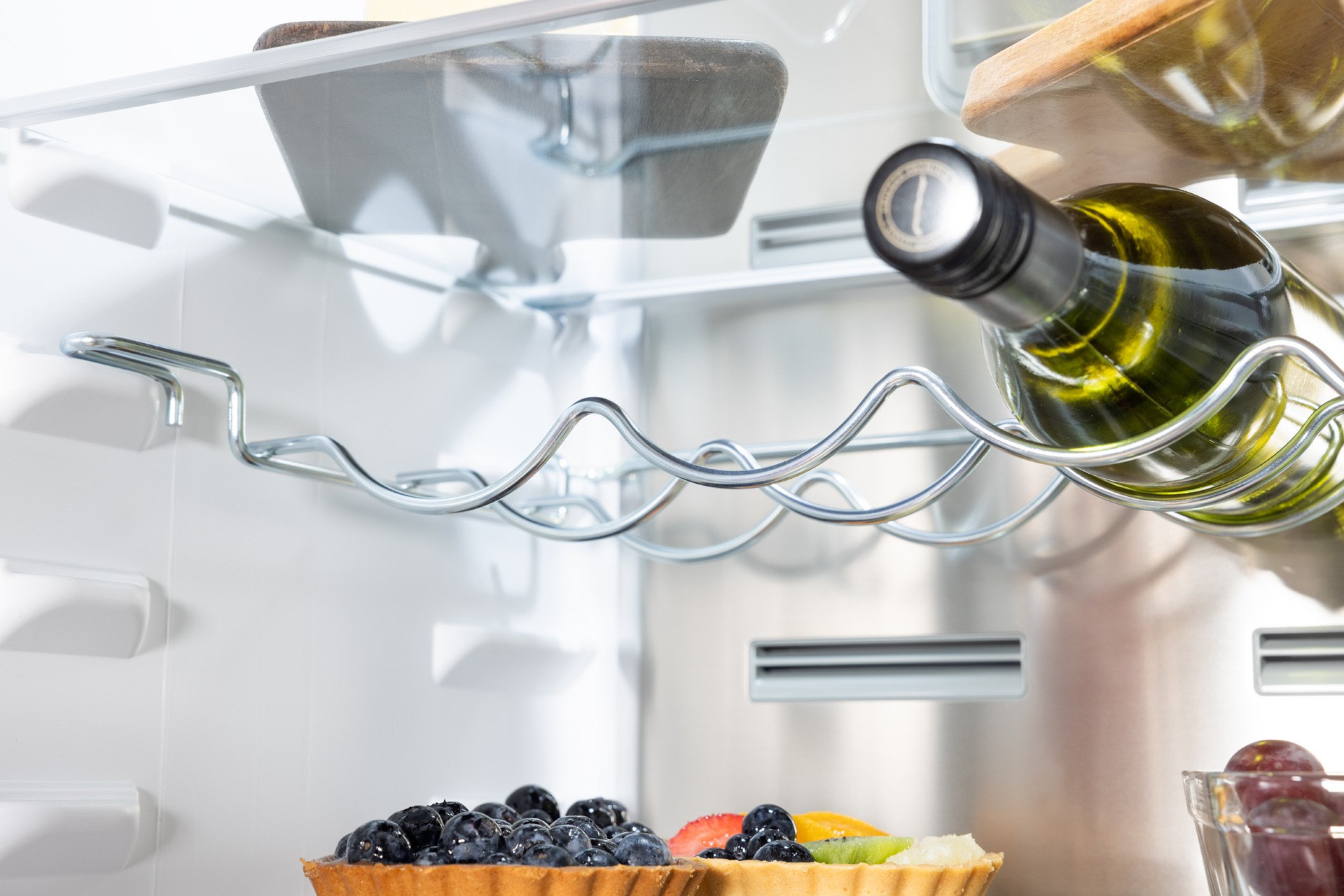 Wnętrze lodówki z butelką wina w uchwycie i tartą owocową.
