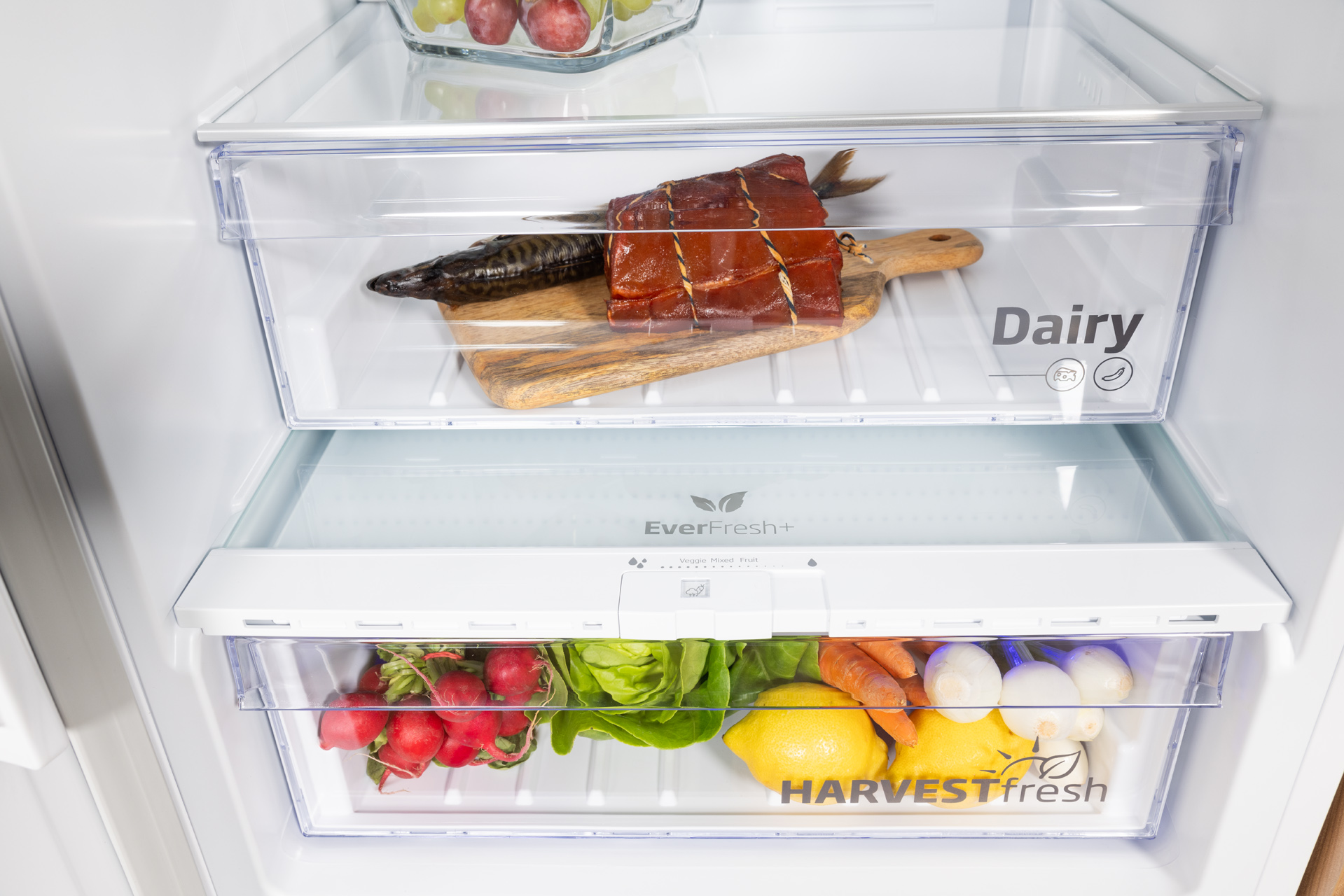 Szuflady lodówki z jedzeniem: wędzona ryba, drewniana deska, rzodkiewki, cytryna i warzywa.