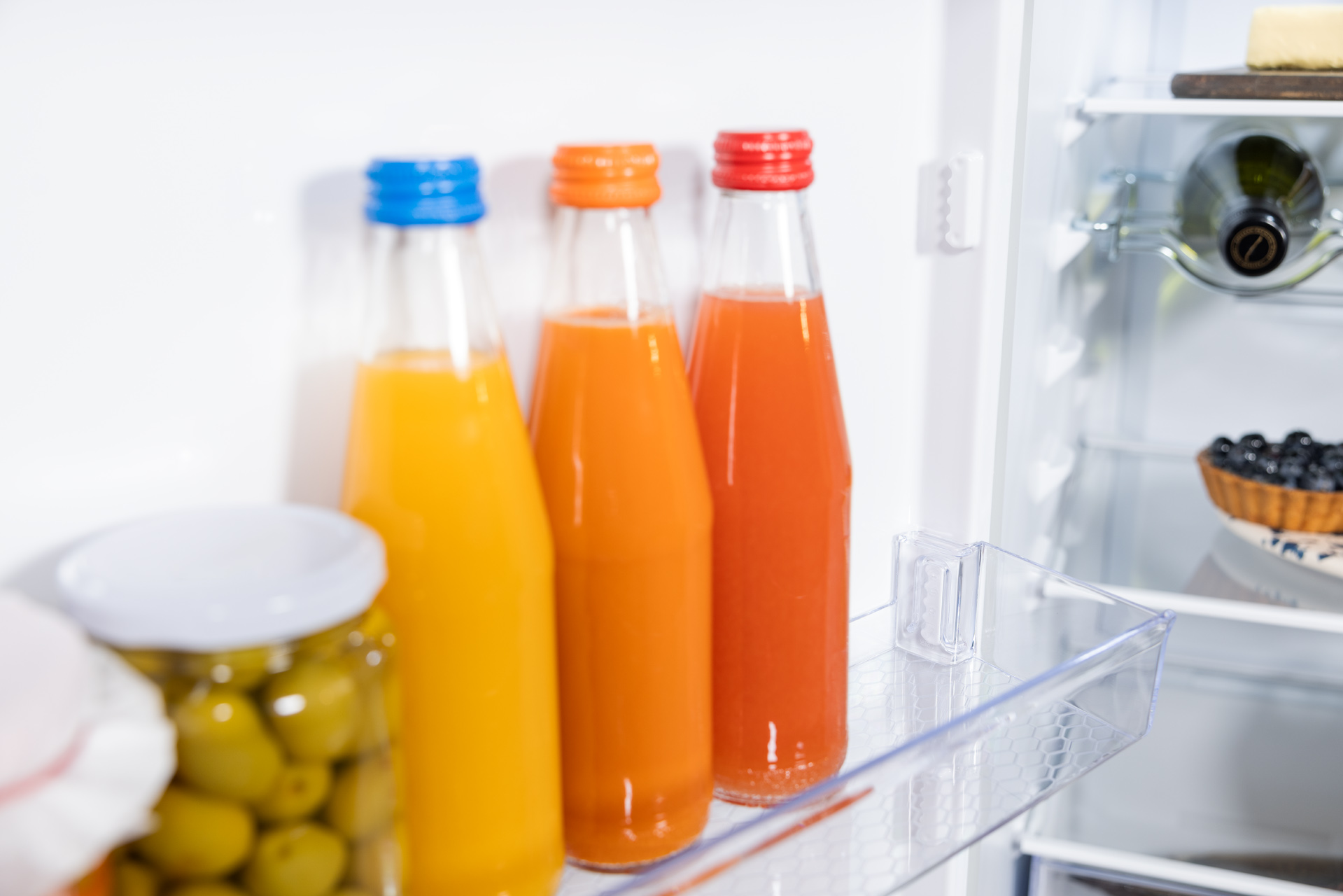Półka w lodówce z trzema butelkami soku. Pomarańczowy, pomarańczowo-czerwony i żółty.