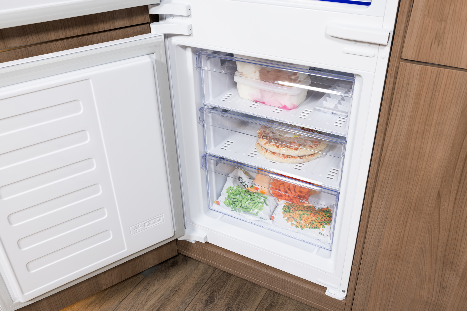 Otwarta lodówka z szufladami zamrażarki zawierającymi mrożonki.