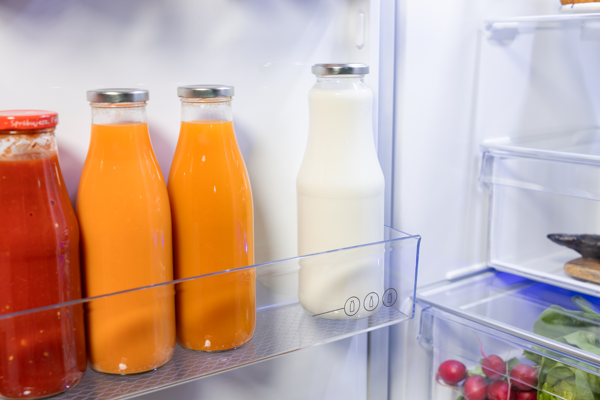 Wnętrze lodówki z butelkami soku i butelką mleka.