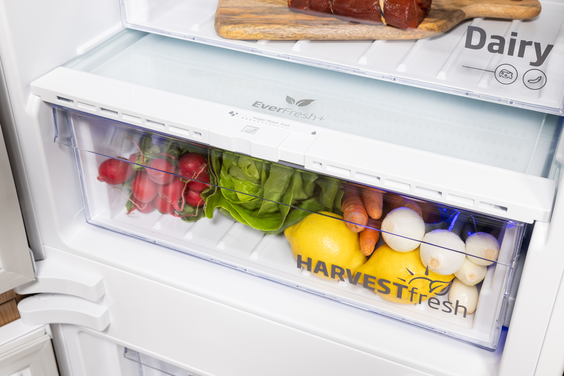 Szuflada lodówki z warzywami i cytryną, etykieta 'harvest fresh'.