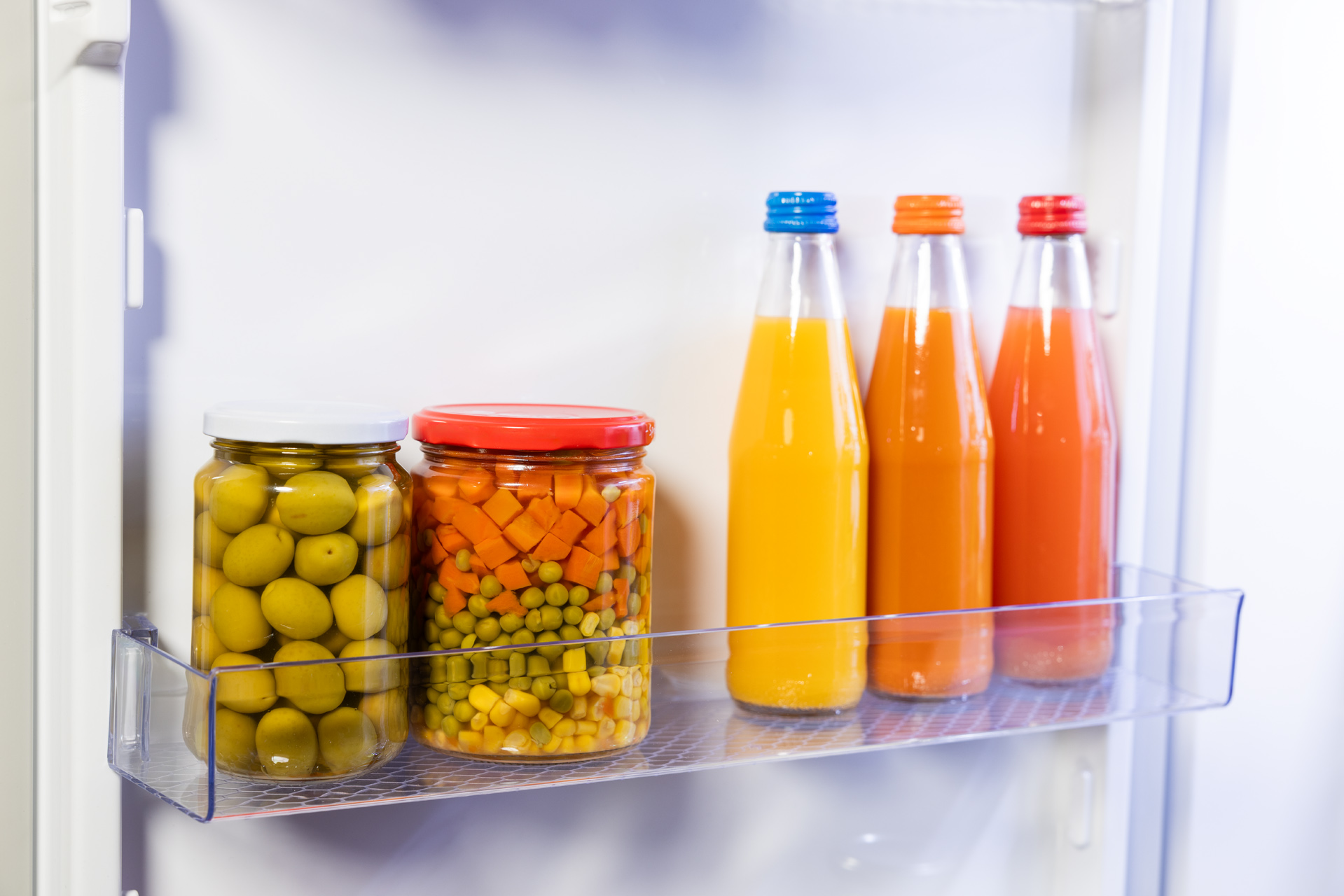 Lodówka ze słoikami oliwek i marynowanych warzyw oraz butelkami soku.