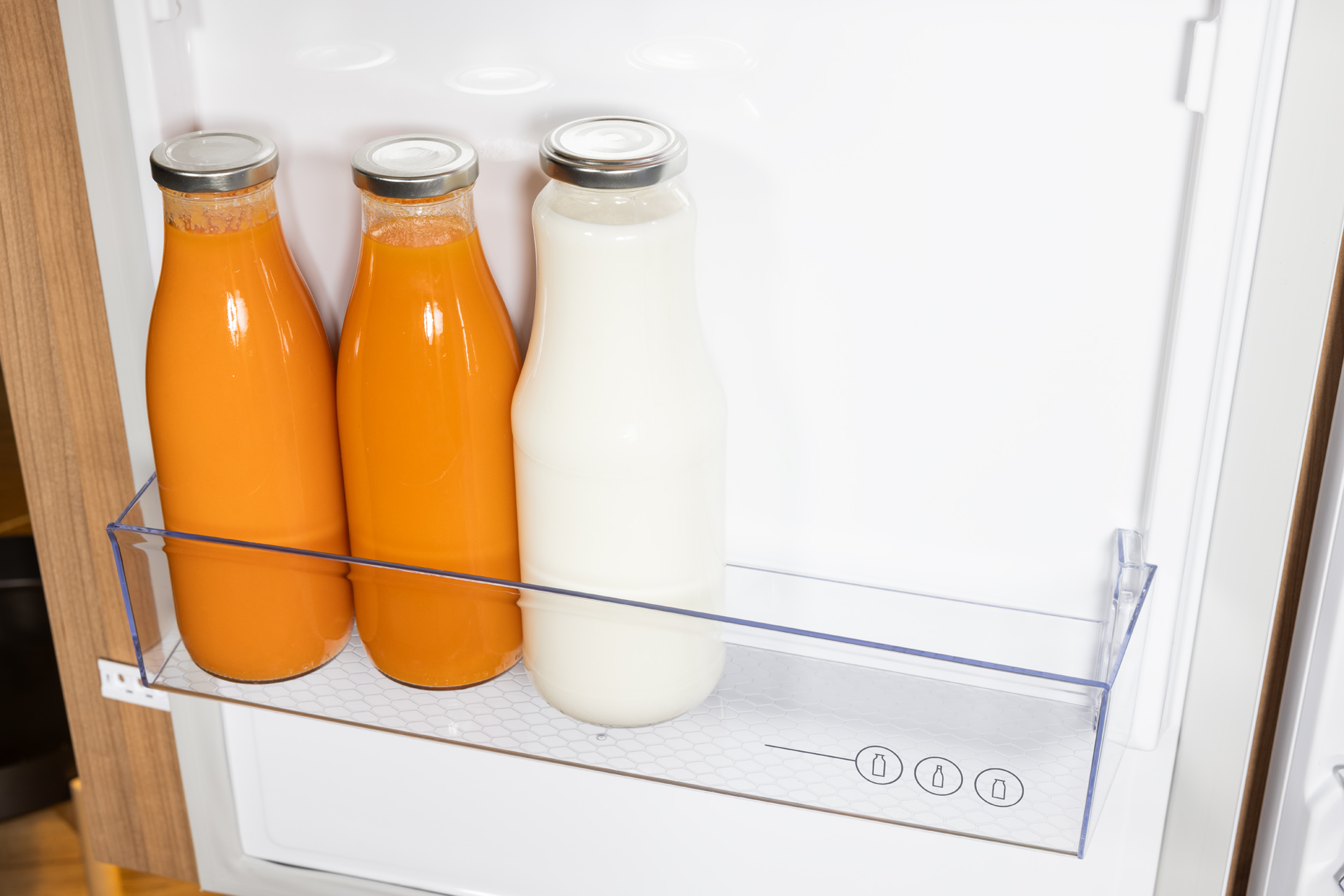 Trzy szklane butelki z płynami na półce w lodówce.