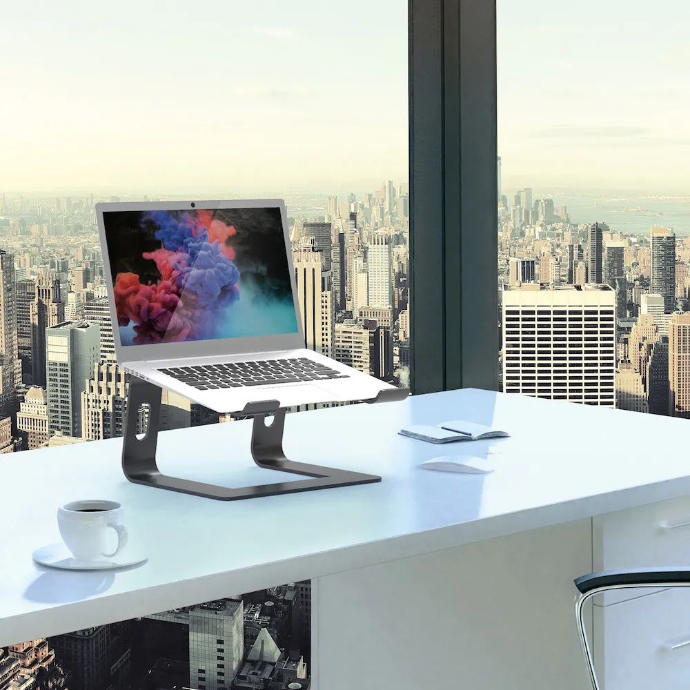 Laptop auf einem Ständer auf einem weißen Schreibtisch mit Stadtansicht. Eine weiße Maus und eine Tasse Kaffee stehen da.