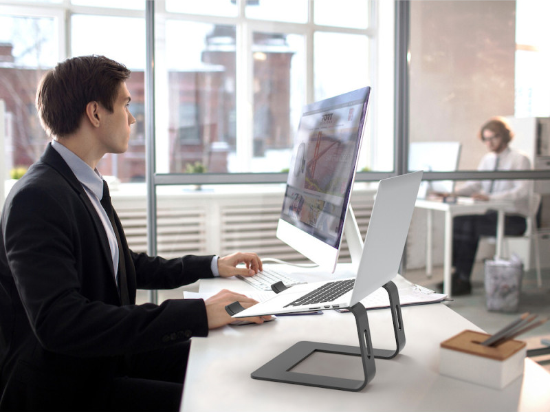Mann benutzt Computer mit Laptopständer, Monitor, Tastatur und Maus auf dem Schreibtisch.