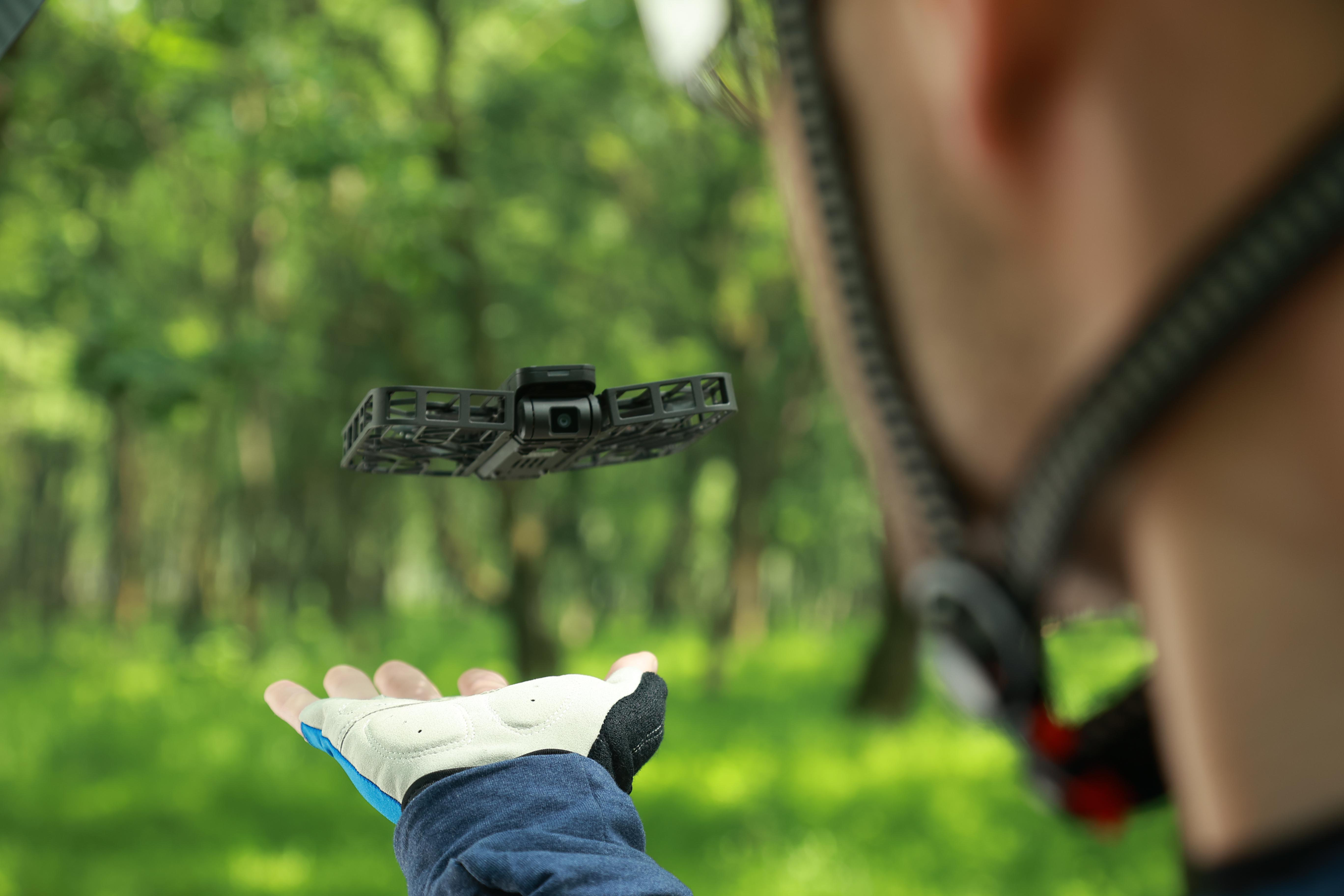 Eine Drohne schwebt vor der Hand einer Person. Die Person trägt einen Helm und Handschuhe.