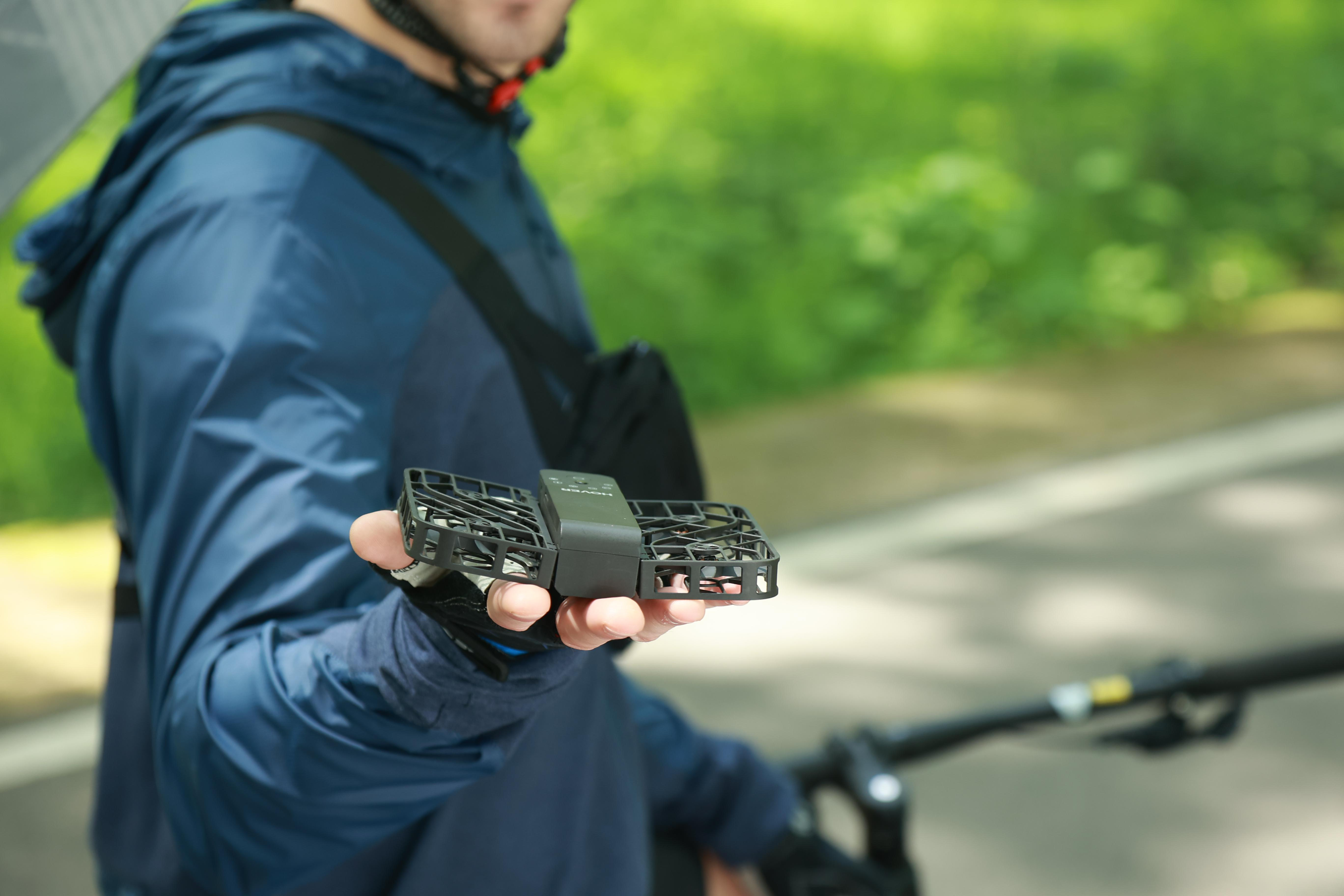 Ein Mann hält eine gefaltete schwarze Drohne, im Hintergrund ein Fahrrad.