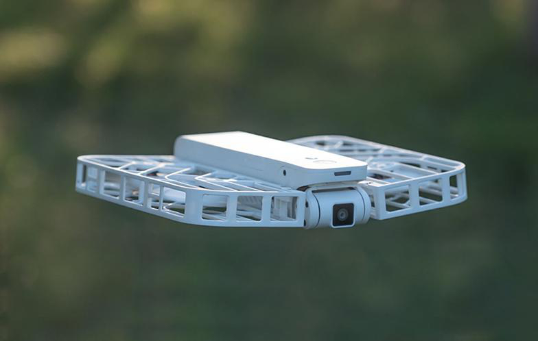 Eine weiße Drohne im Flug, leicht nach unten geneigt, mit verschwommenem grünem Hintergrund.