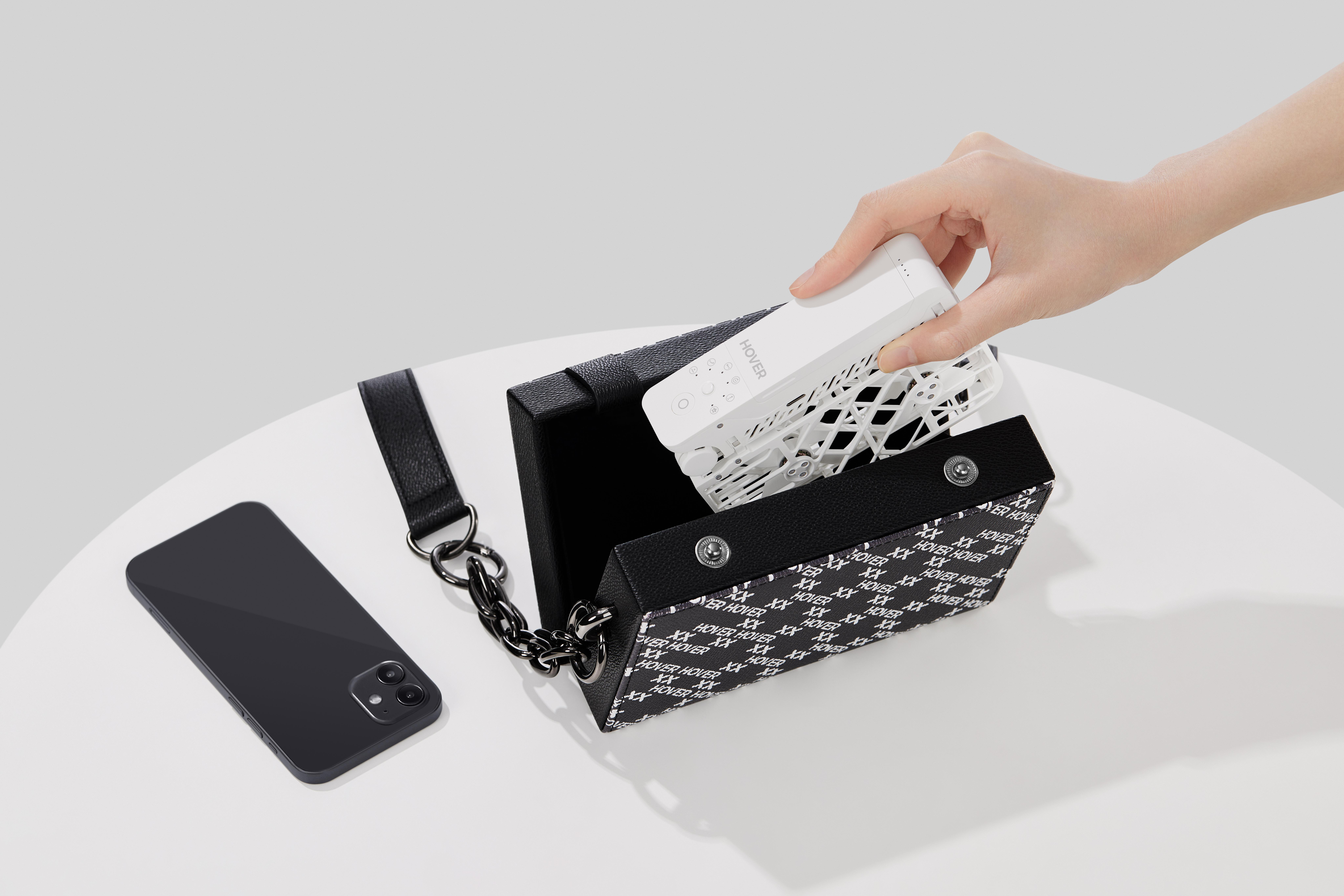 Eine Hand, die eine weiße Drohne aus einer schwarz-weiß gemusterten Handtasche nimmt.