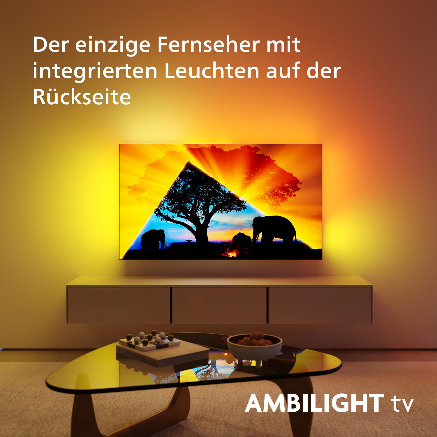 Fernseher mit einer Szene mit Elefanten und einem Baum. Umgebungslicht an der Wand. Text: AMBILIGHT tv.