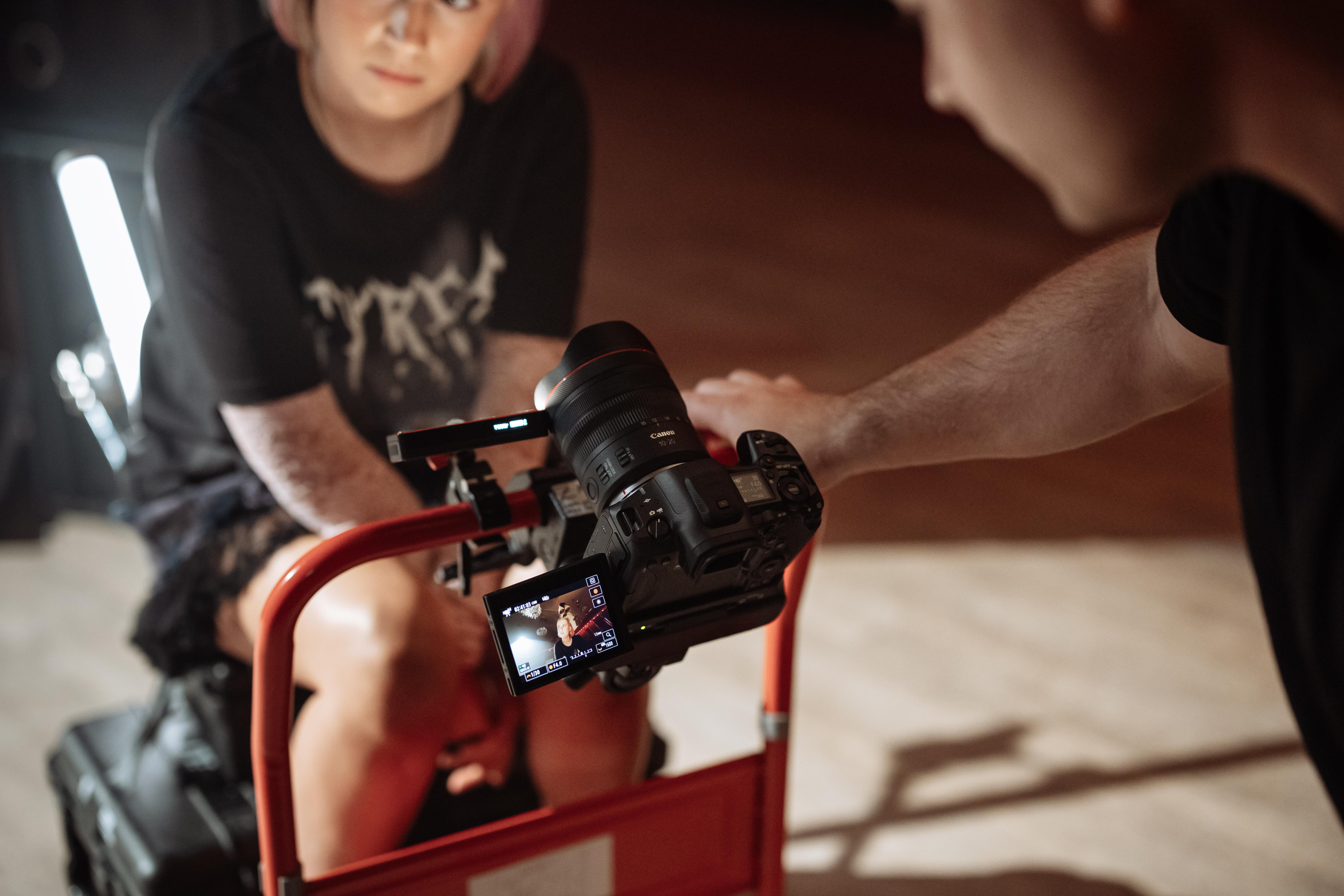 Eine Person filmt eine andere Person mit einer Kamera auf einem Dolly. Beide sind drinnen.