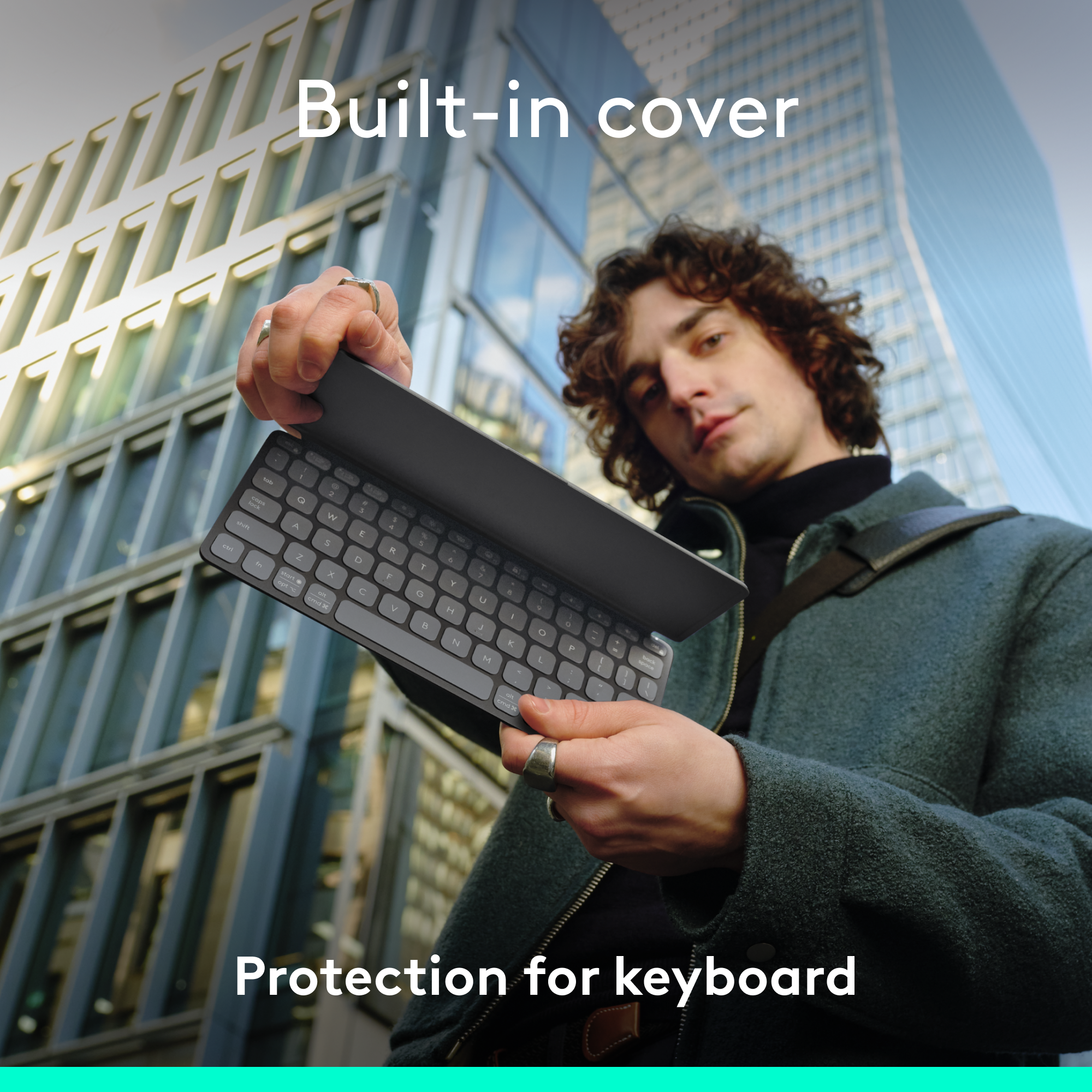 Ein Mann hält eine dunkle Tastatur mit integrierter Abdeckung, Stadtbild im Hintergrund.