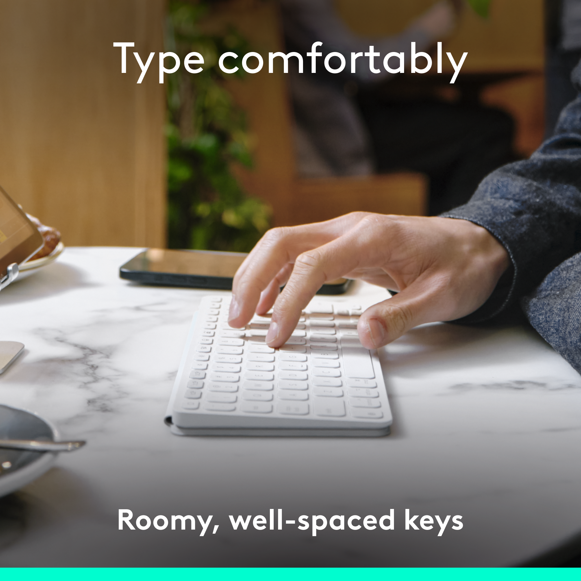 Person tippt auf einer weißen Tastatur. Gut verteilte Tasten, Telefon, Schreibtisch.