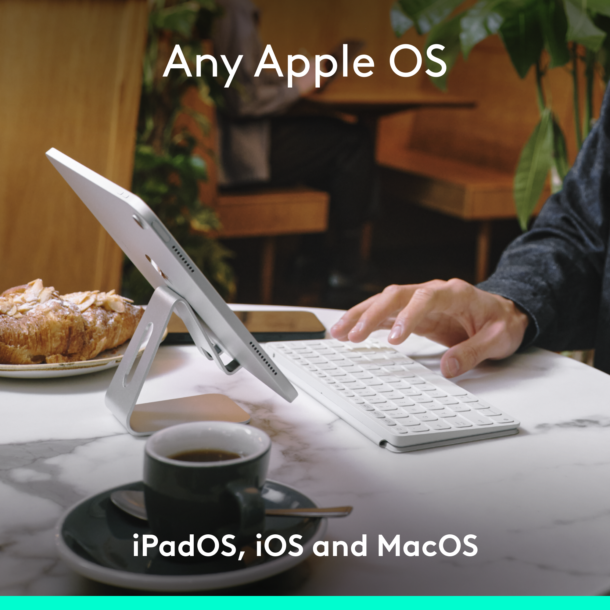 Ein iPad auf einem Ständer mit Tastatur und Kaffee. Es liegt neben einem Croissant. Der Text lautet 'Any Apple OS'.