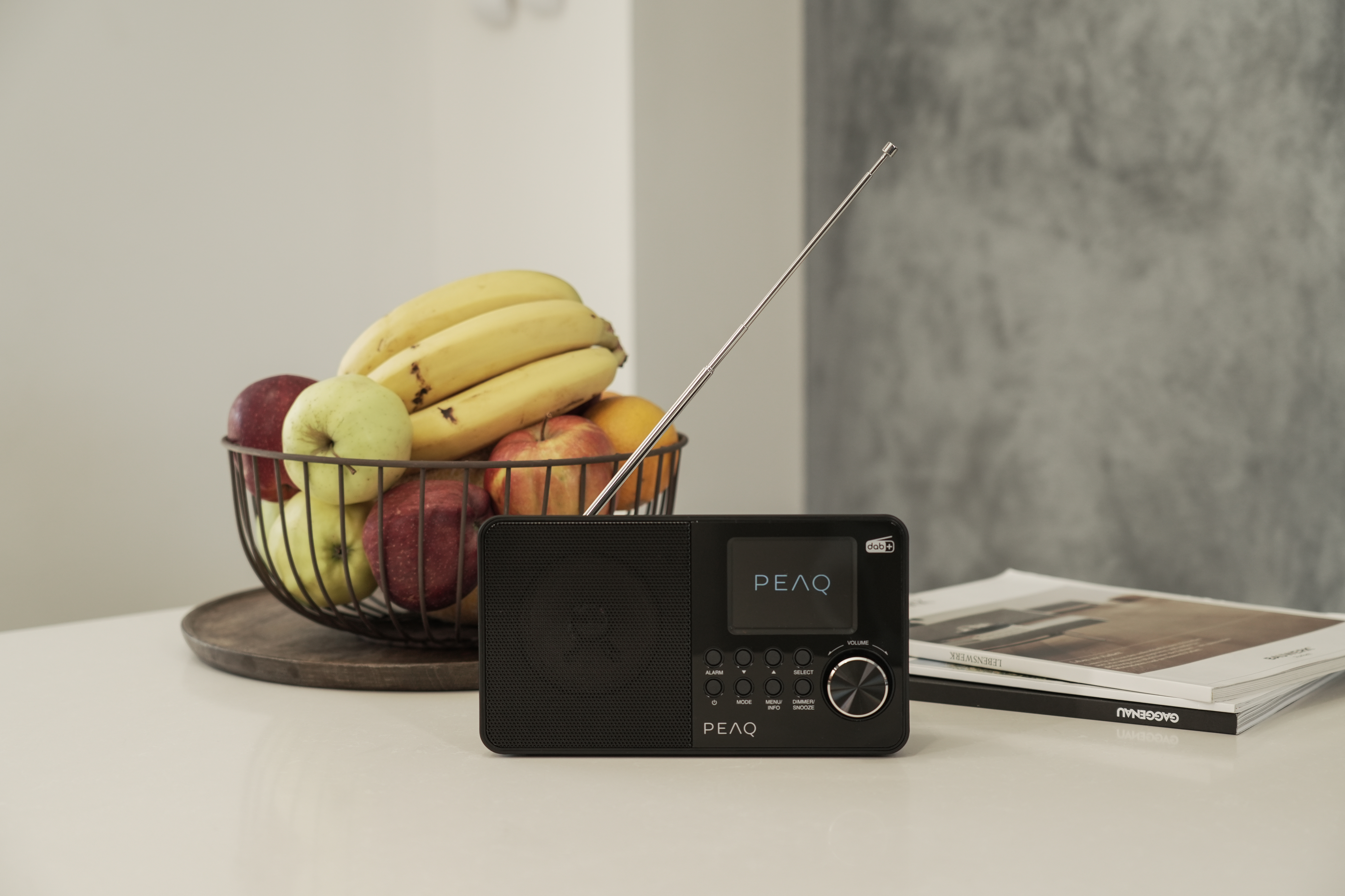 Une radio noire avec un écran et un panier de fruits sur une table blanche.