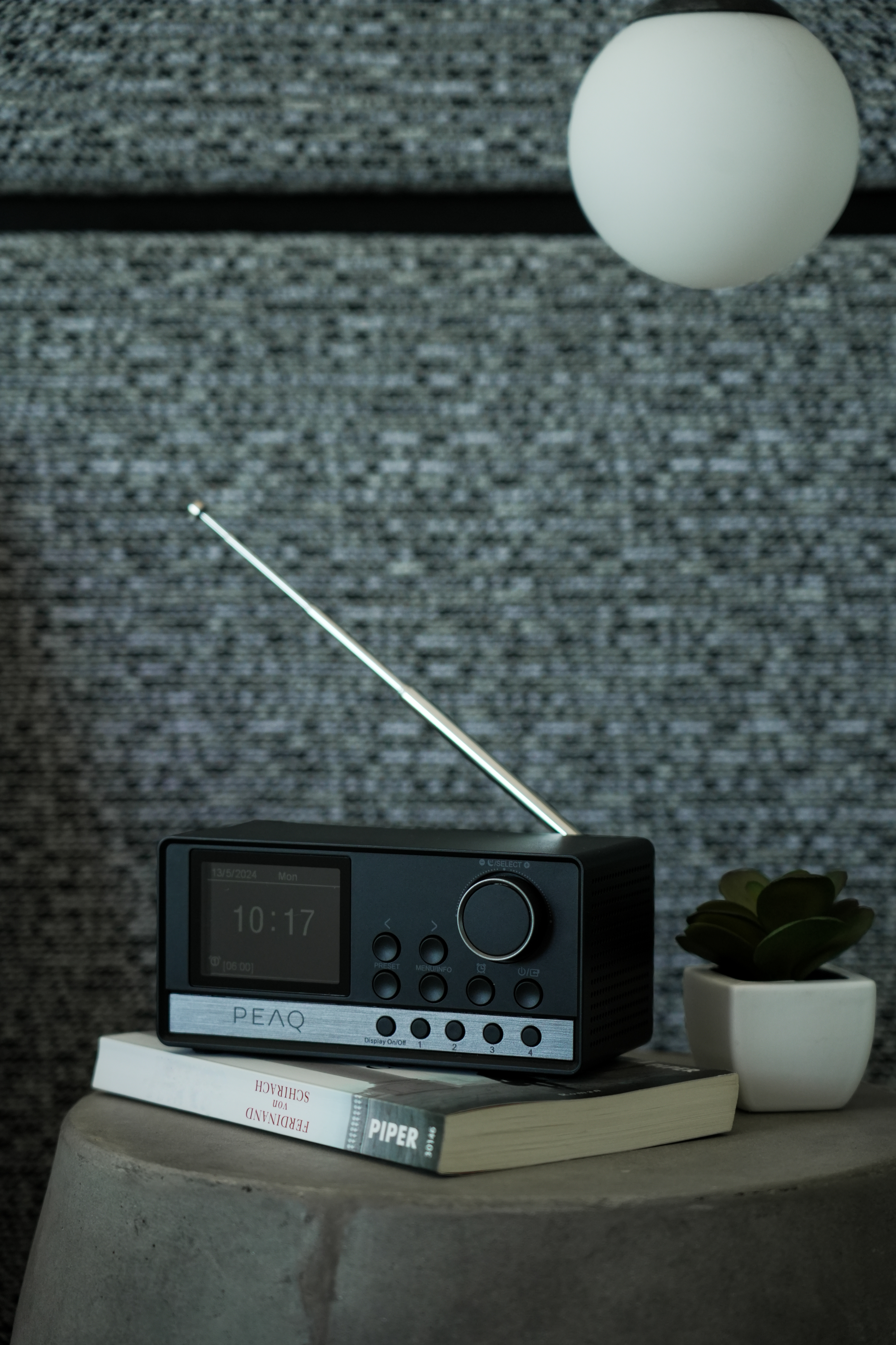 Une radio noire avec un affichage numérique et une antenne est posée sur des livres, sur une surface en forme de pierre.