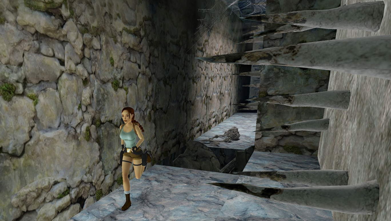 Lara Croft rennt in einem Steinkorridor mit Stacheln. Der Korridor hat eine Steinmauer und einen dunklen Hintergrund.