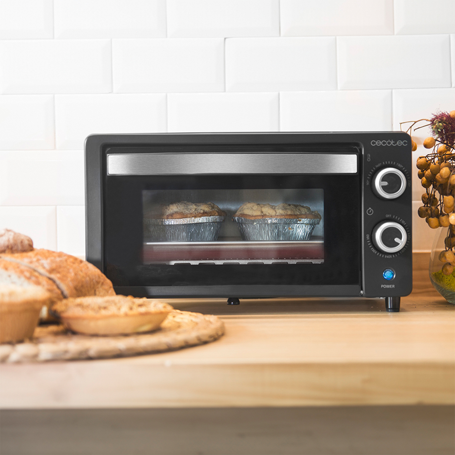 Un piccolo forno nero con due torte in cottura. Altri alimenti su una superficie di legno.