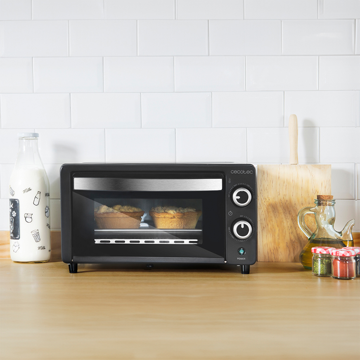 Un mini forno nero su un piano di lavoro in legno con prodotti da forno e utensili da cucina.