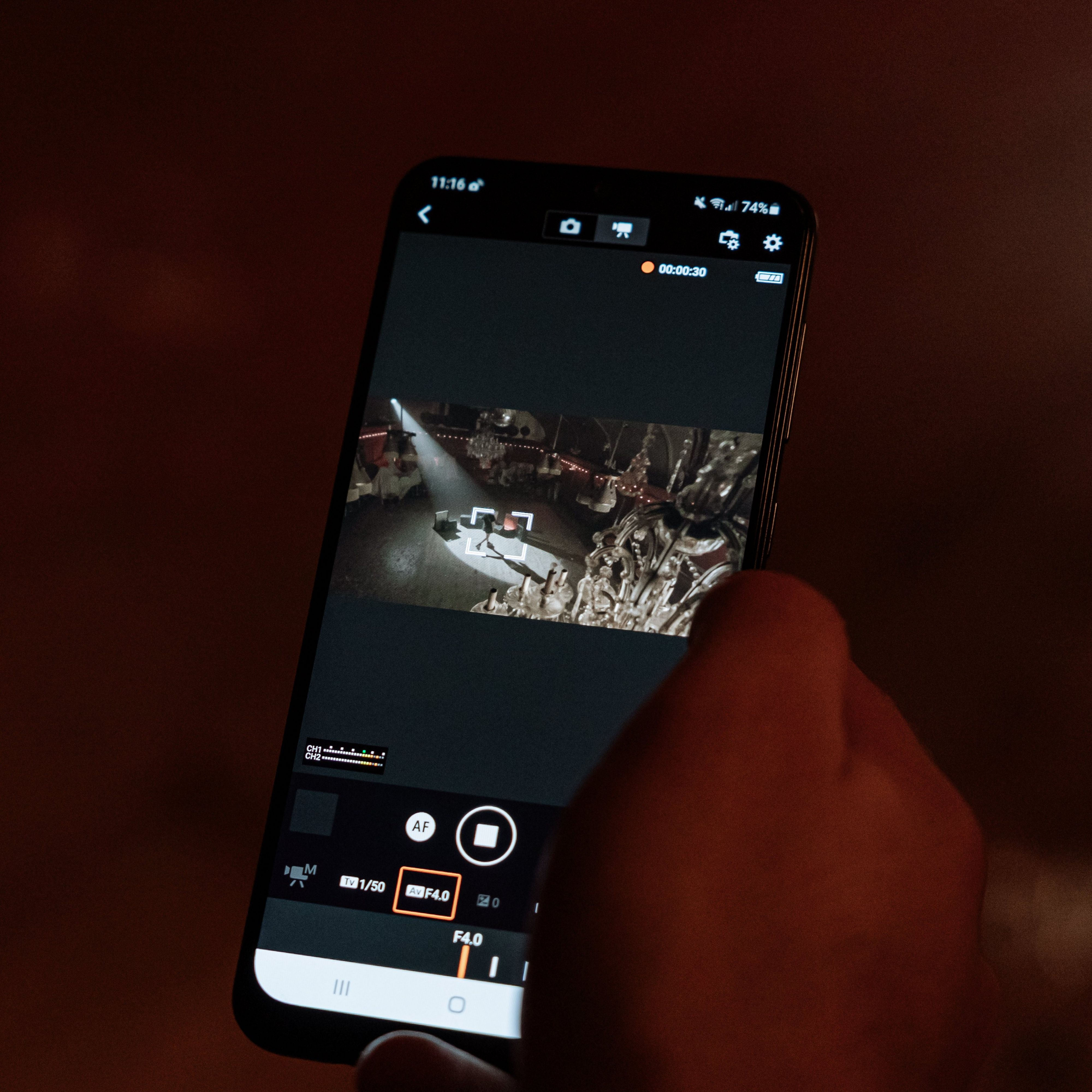 Une main tenant un smartphone, affichant une interface de caméra de drone avec des commandes d'enregistrement.