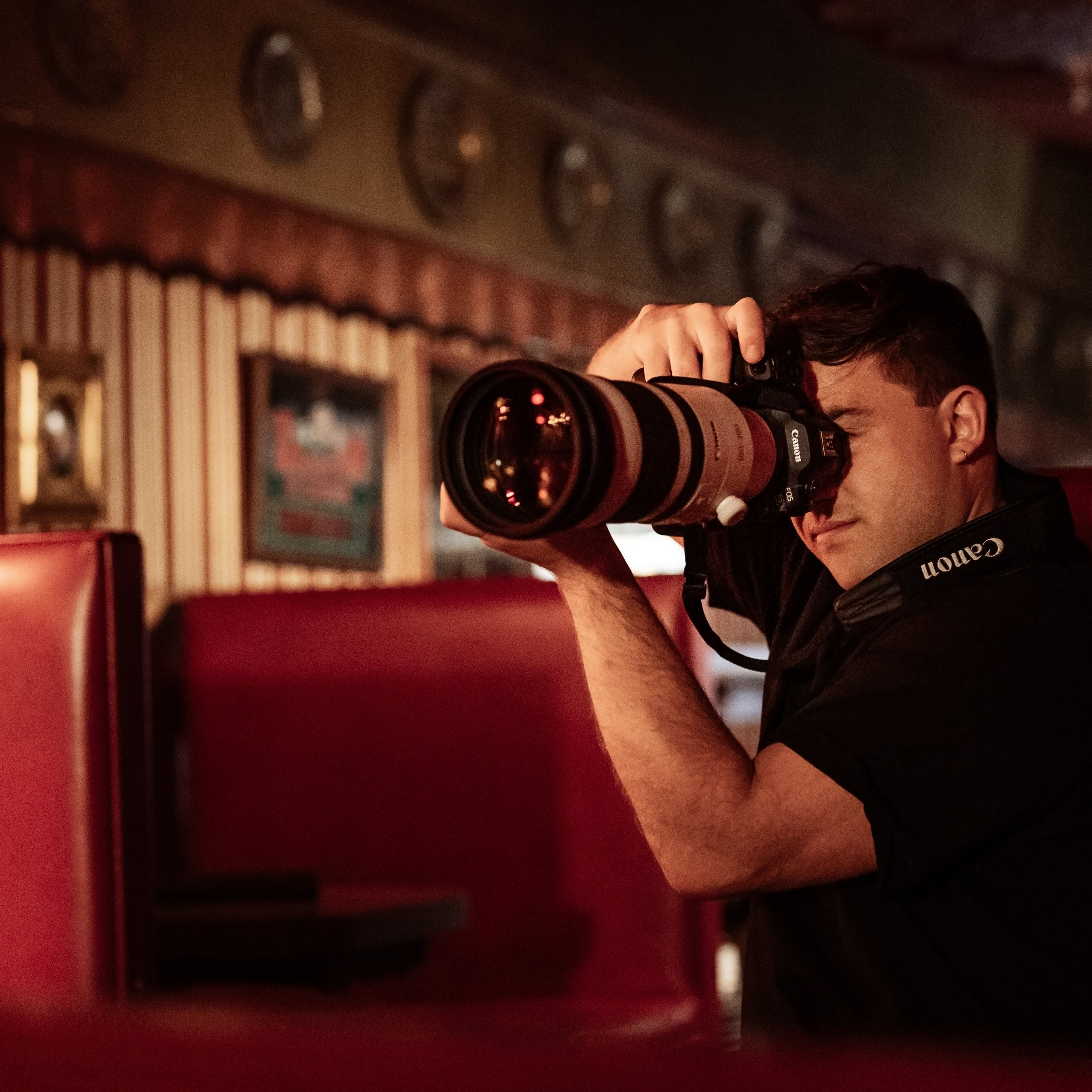 Un homme prend une photo avec un appareil photo Canon dans un stand de restaurant. L'appareil photo a un grand objectif.
