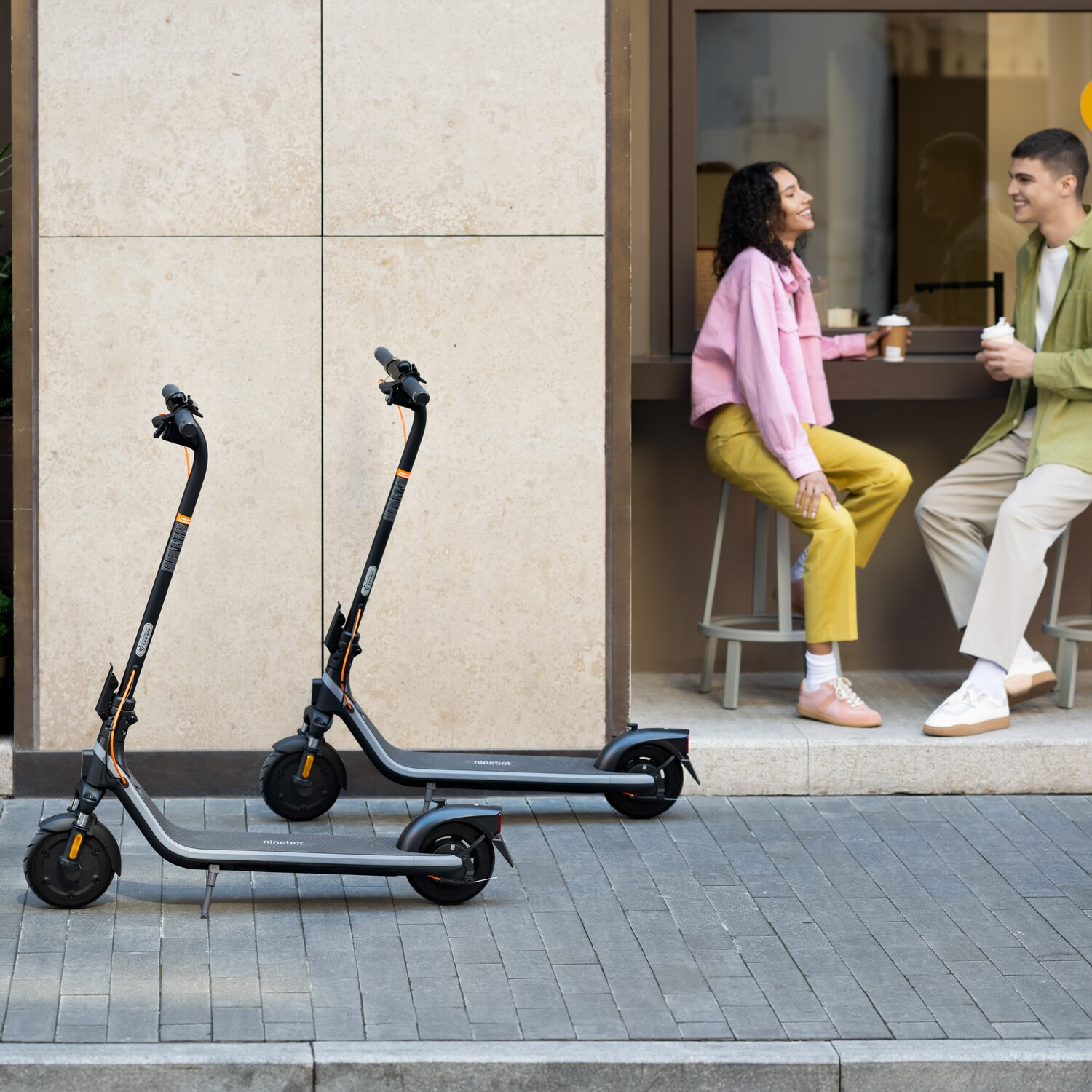 Two scooters parked on a sidewalk. A couple is sitting at a table in the background.