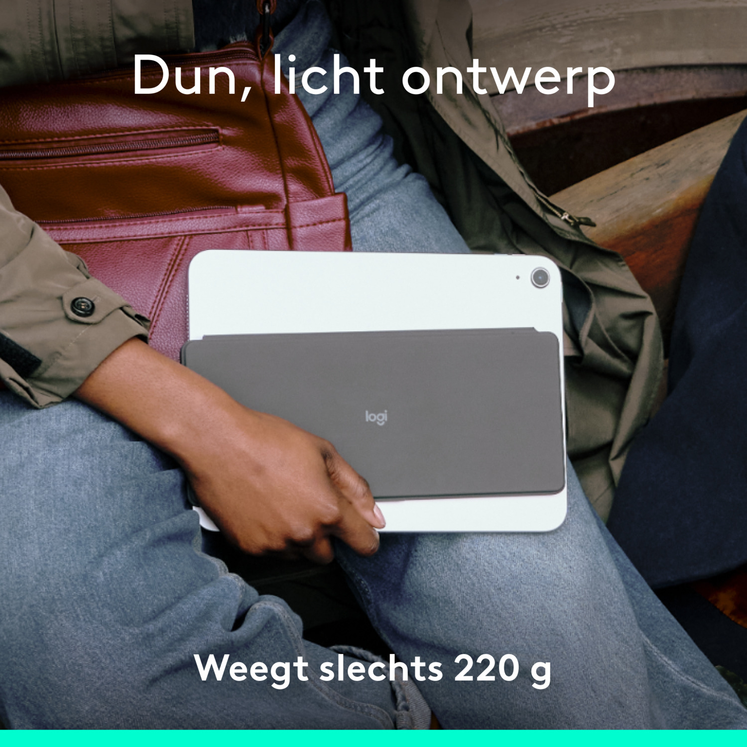 A person holding a white tablet with a grey keyboard cover, against a person's legs and a bag.