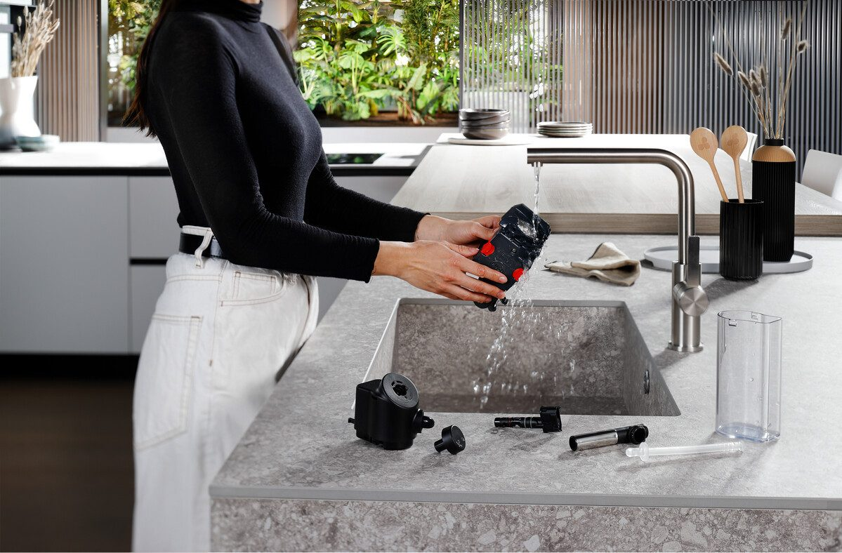 Kobieta myjąca czarne części urządzenia w zlewie. Otoczenie kuchni.