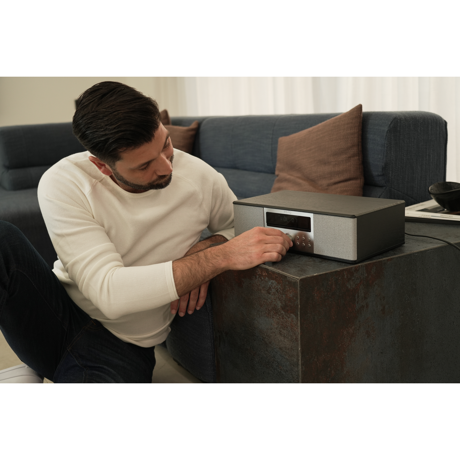 Man sitting adjusts the knob on a black and silver radio.