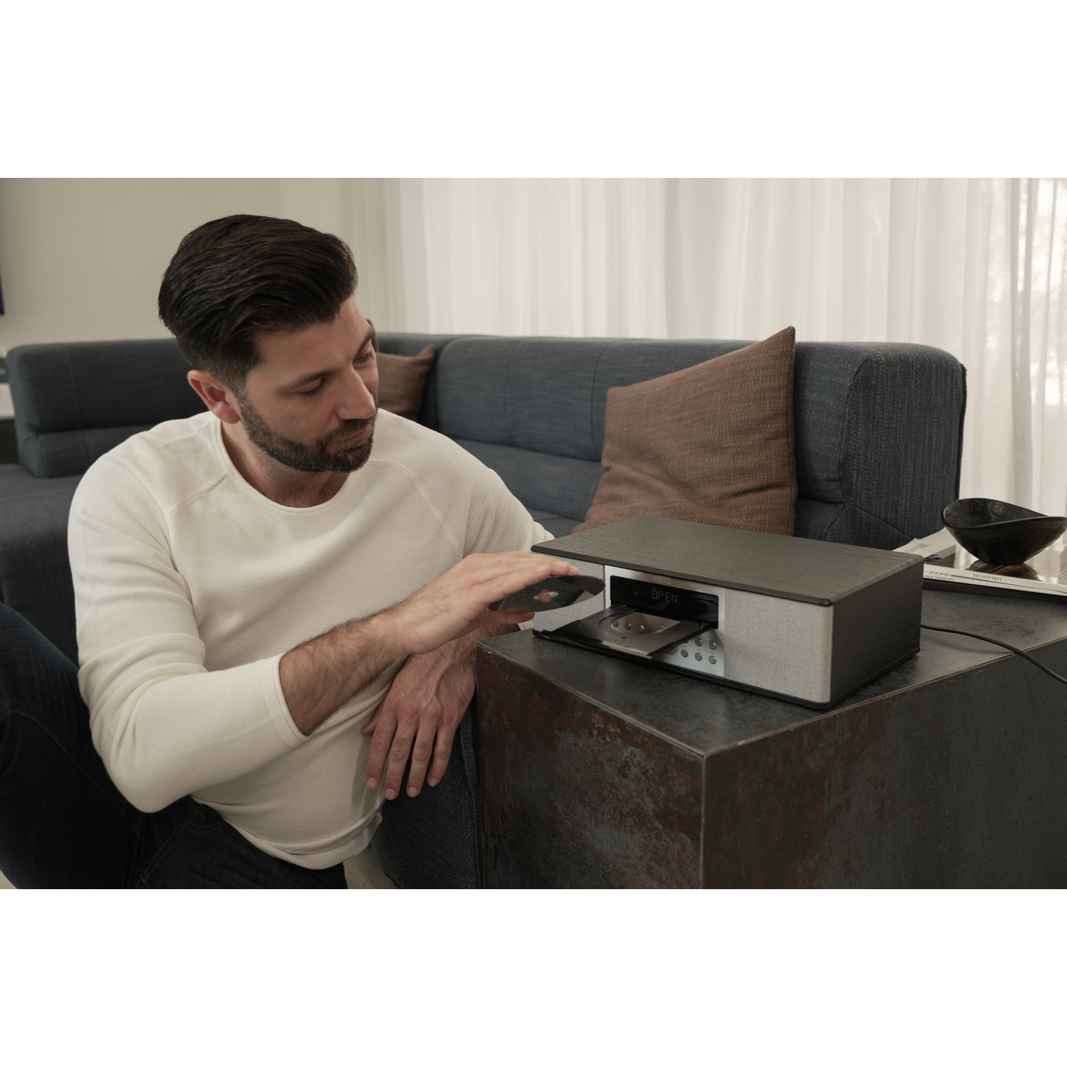 A man is operating a CD player. The CD player is on a dark surface.