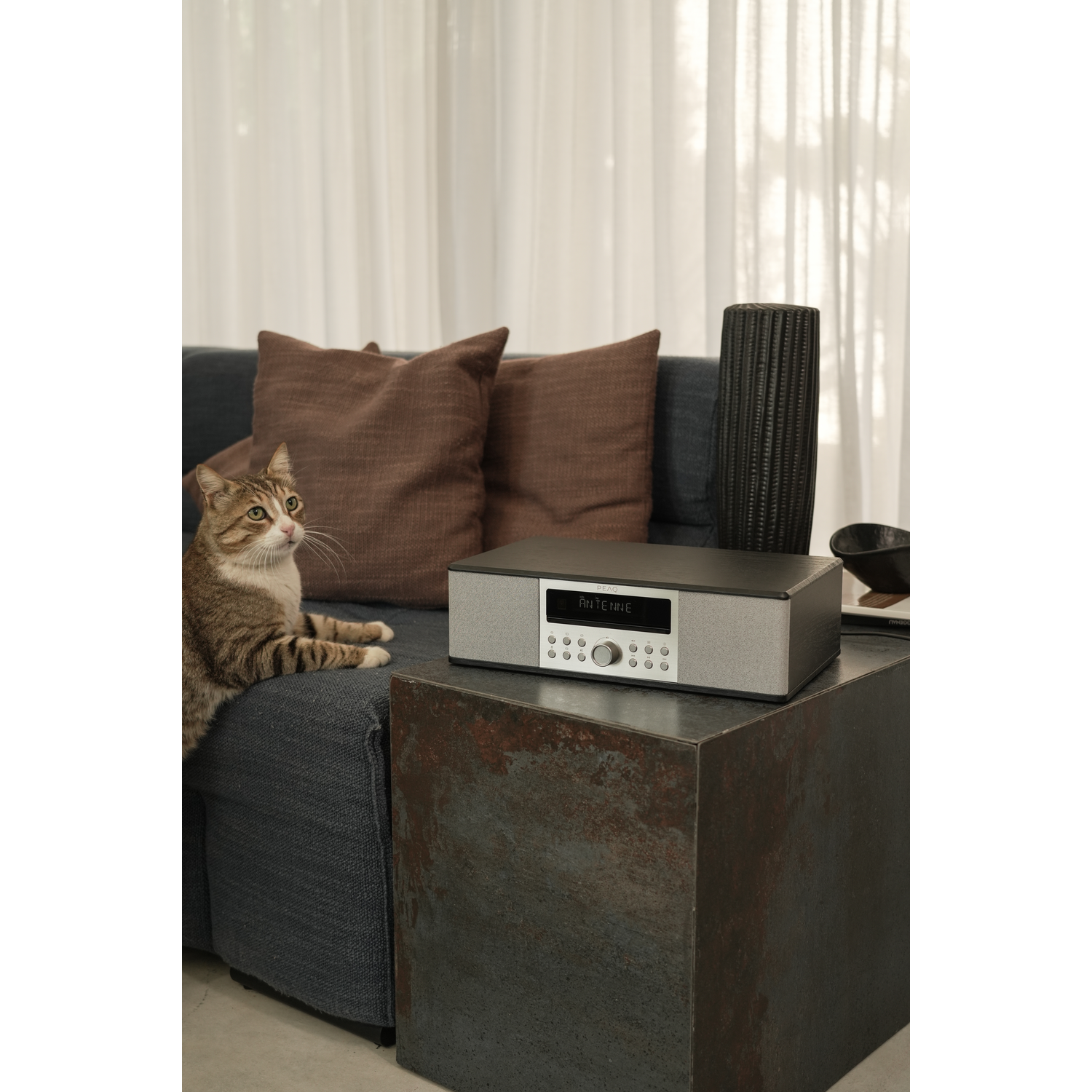 A cat sits on a blue couch next to a stereo system on a metal side table.