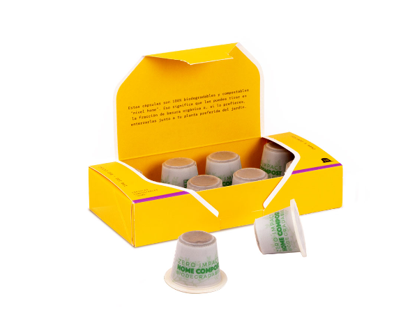 Una caja de cápsulas de café biodegradables. Caja amarilla y cápsulas grises. Fondo blanco.