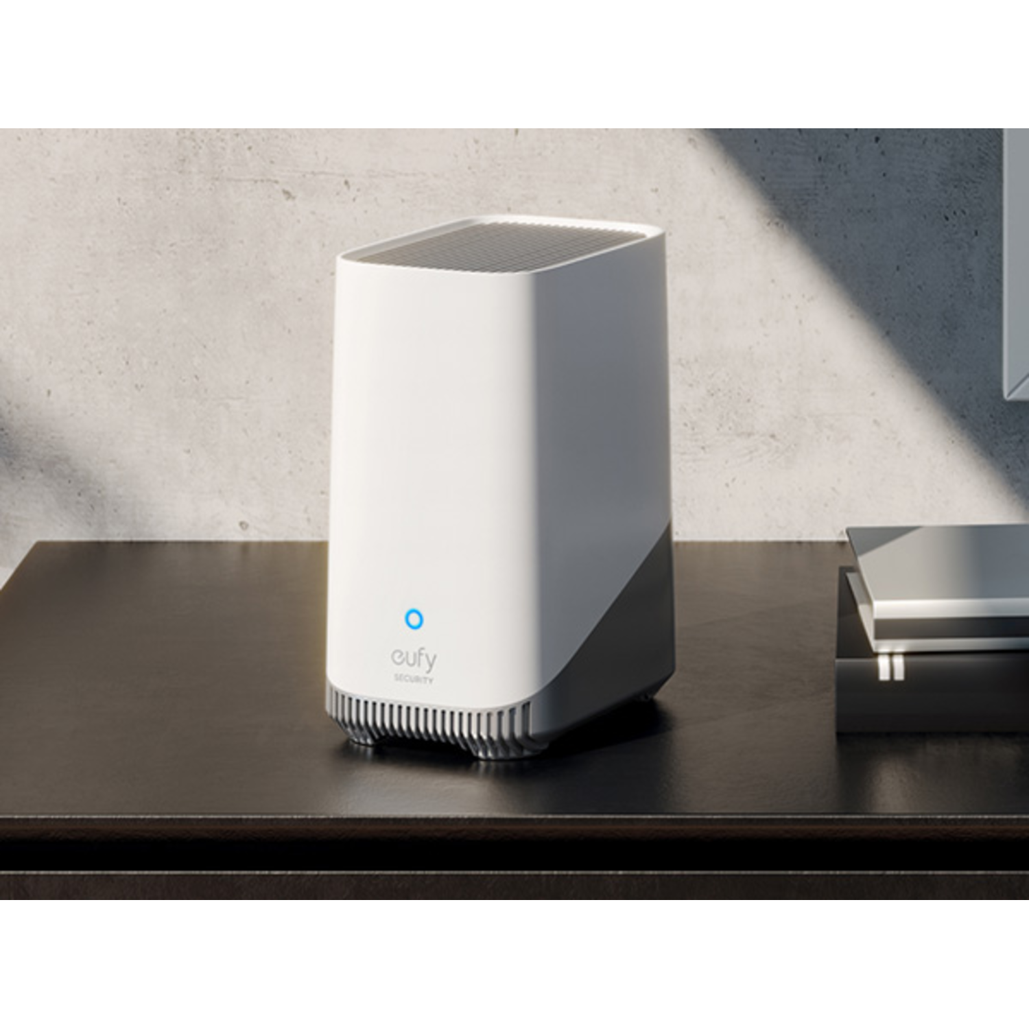 A white and gray eufy security device on a dark wooden table, with a blue light.