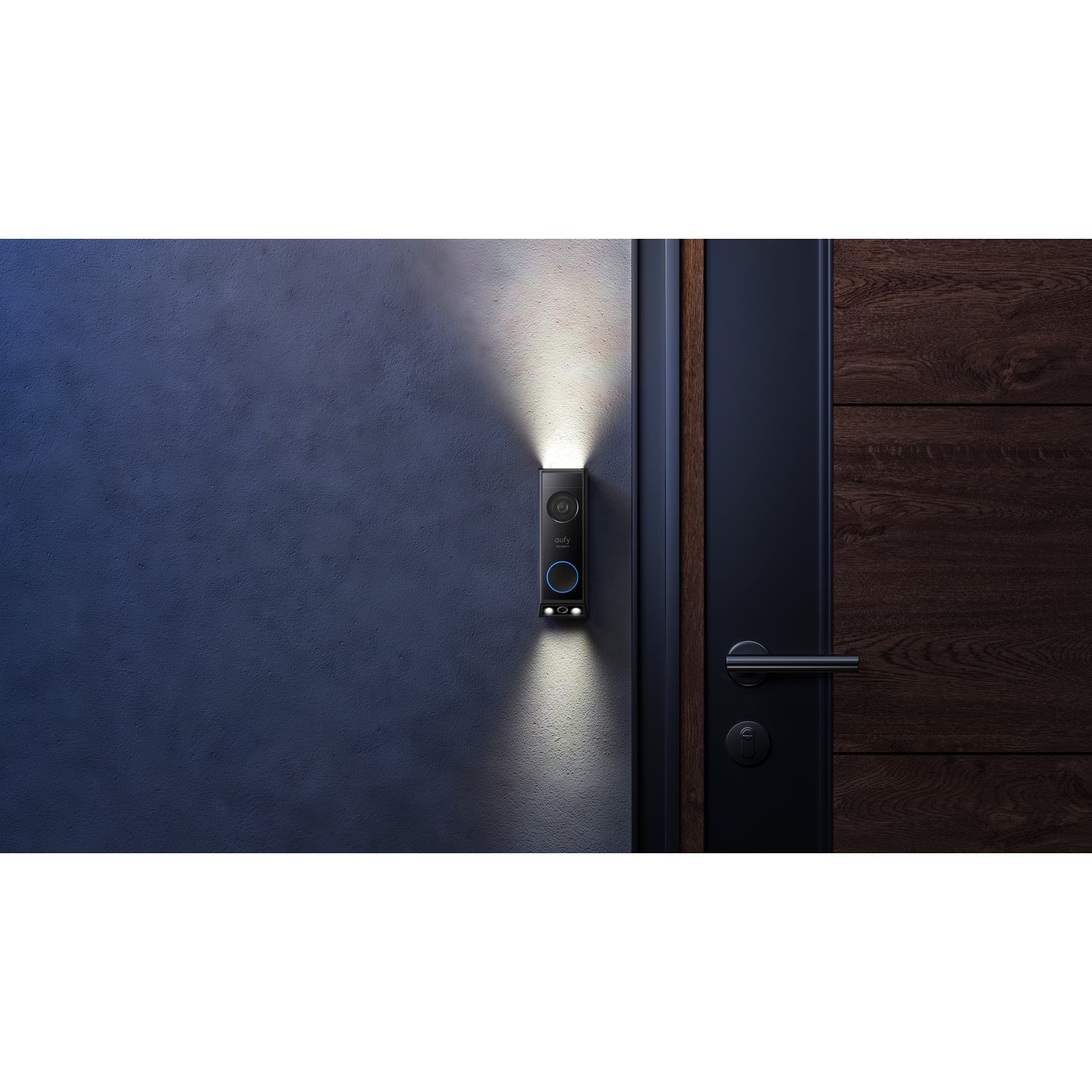 A black doorbell on a dark wall, lit by two lights. A wooden door is in the background.