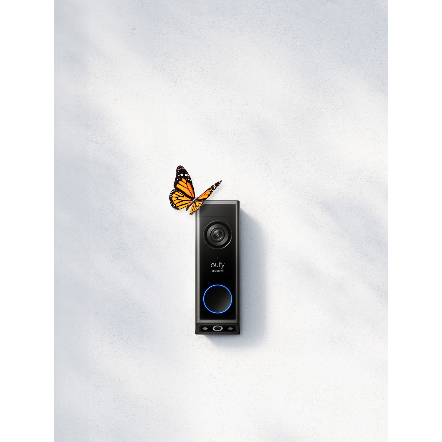 Black doorbell with a butterfly on it, mounted on a white wall.