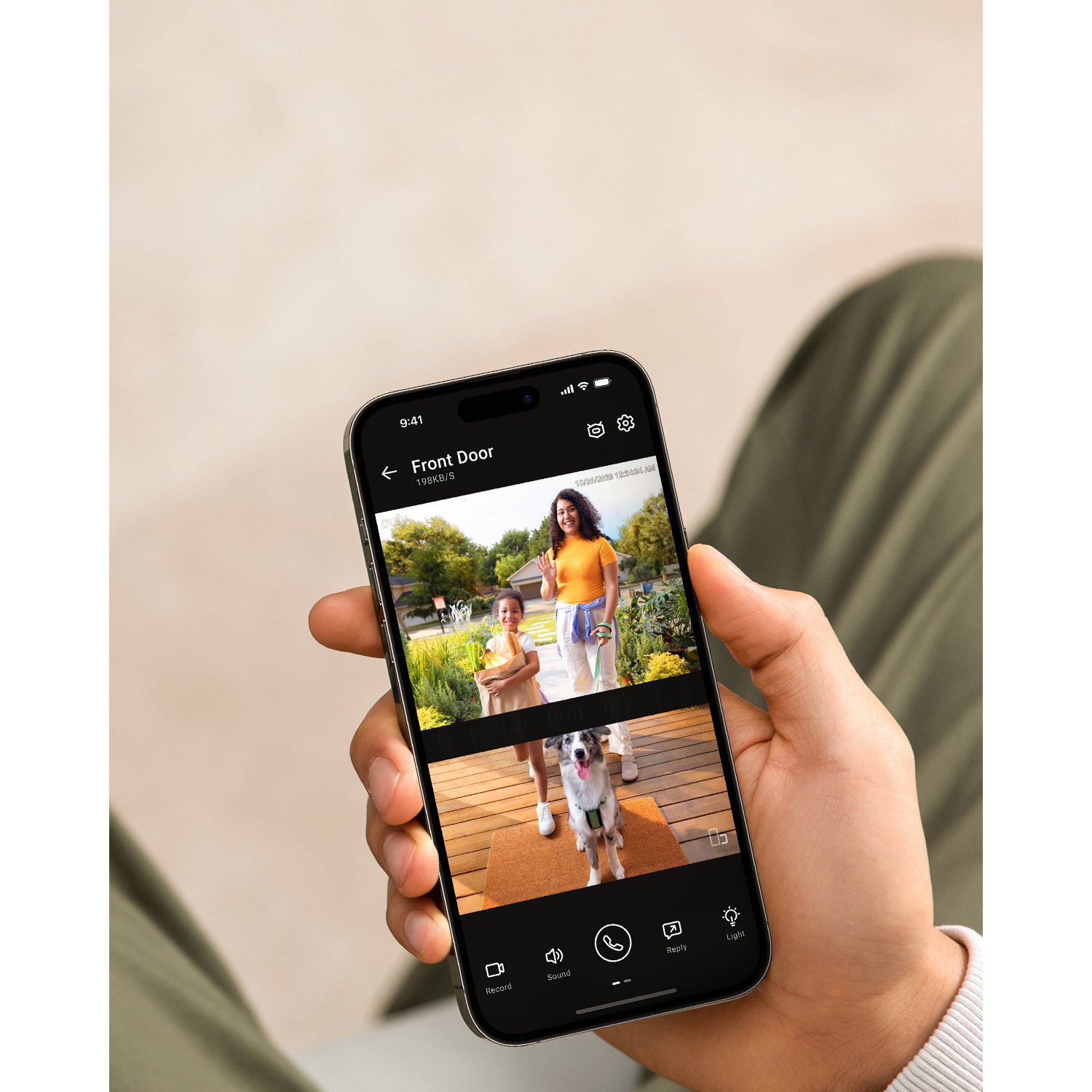 A person holding a phone displaying a video feed of a woman and child, and a dog on a doormat.