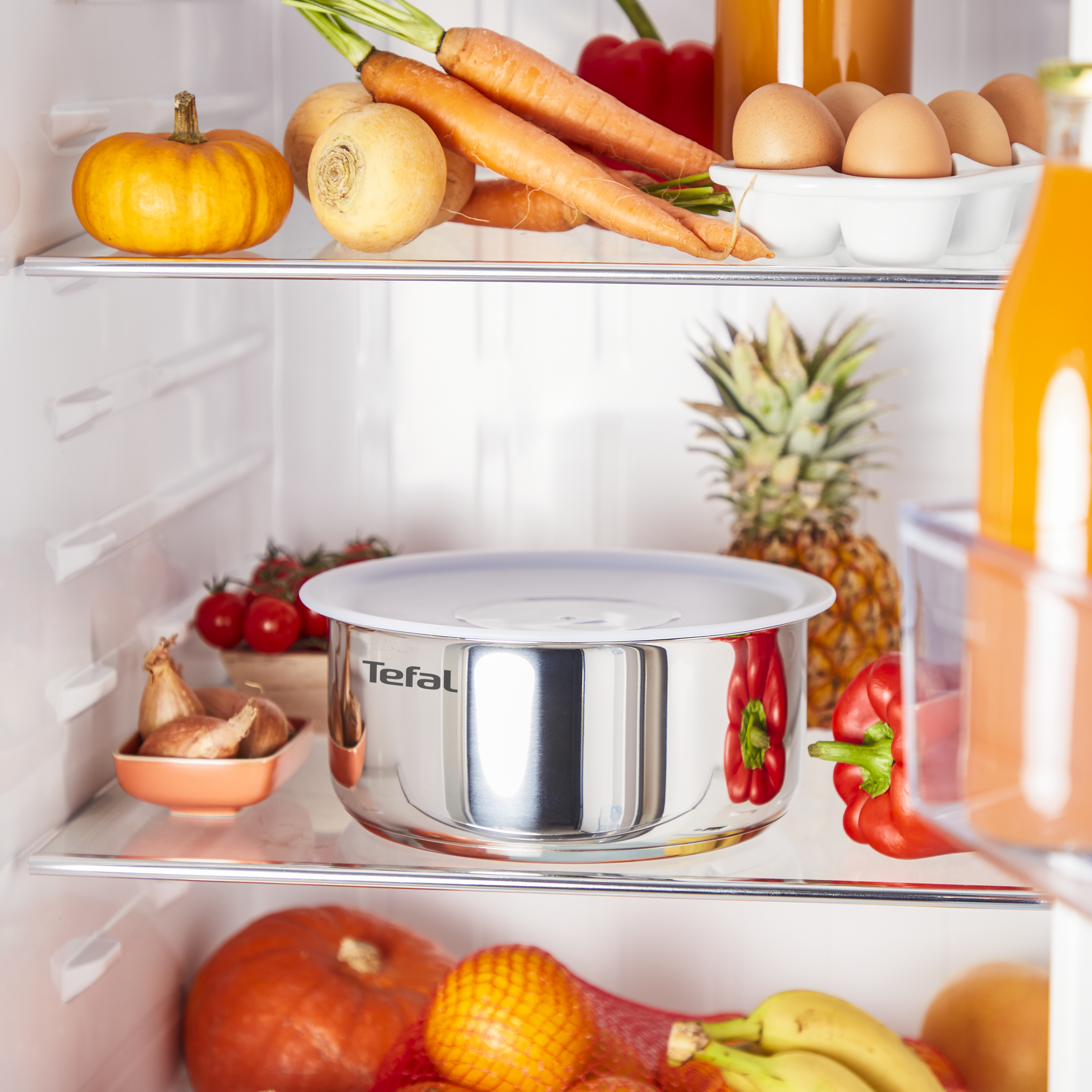 Otwarta lodówka z różnymi produktami spożywczymi w środku, w tym warzywami, jajkami i owocami.