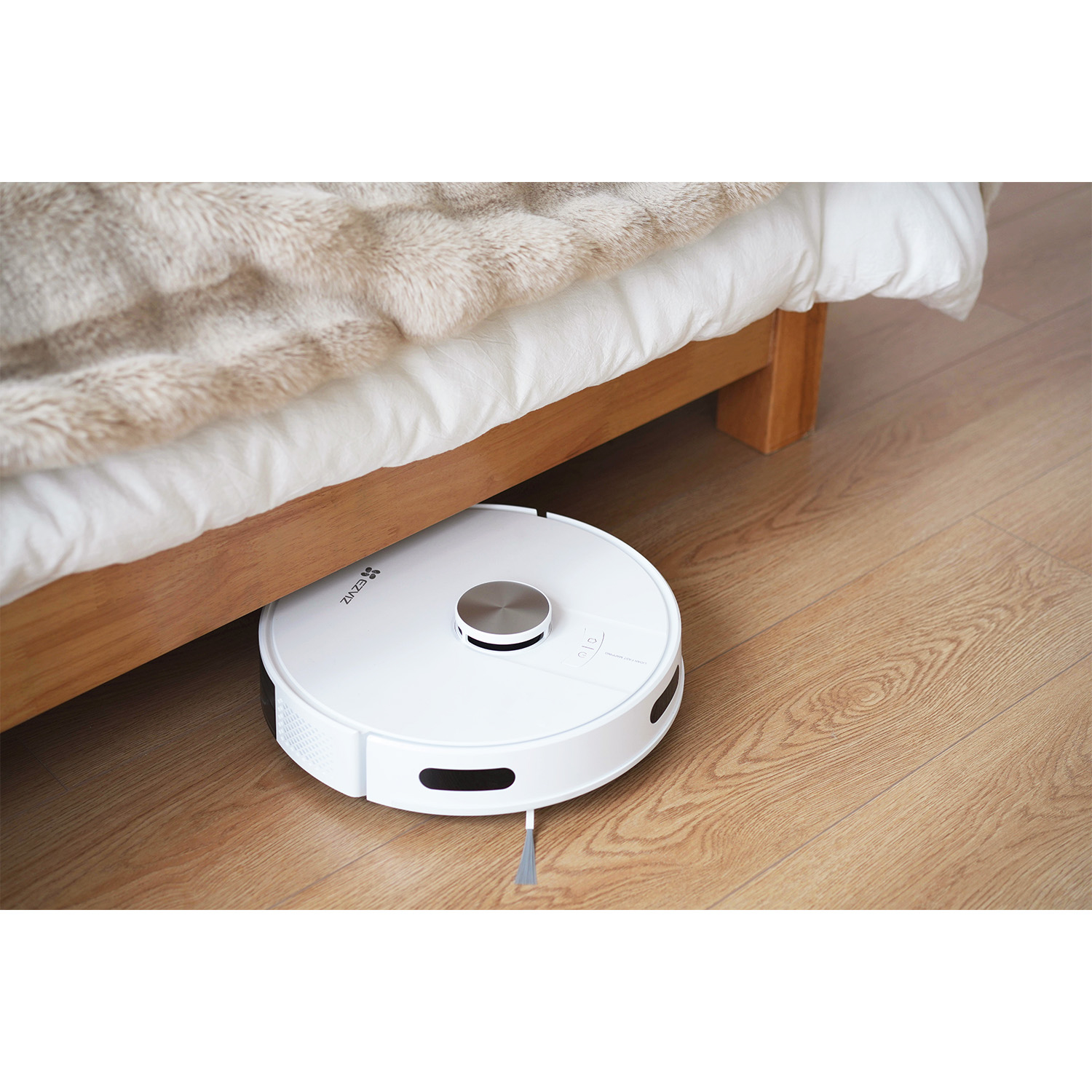 Un aspirapolvere robot bianco è posizionato sotto un letto. Il pavimento è in legno.