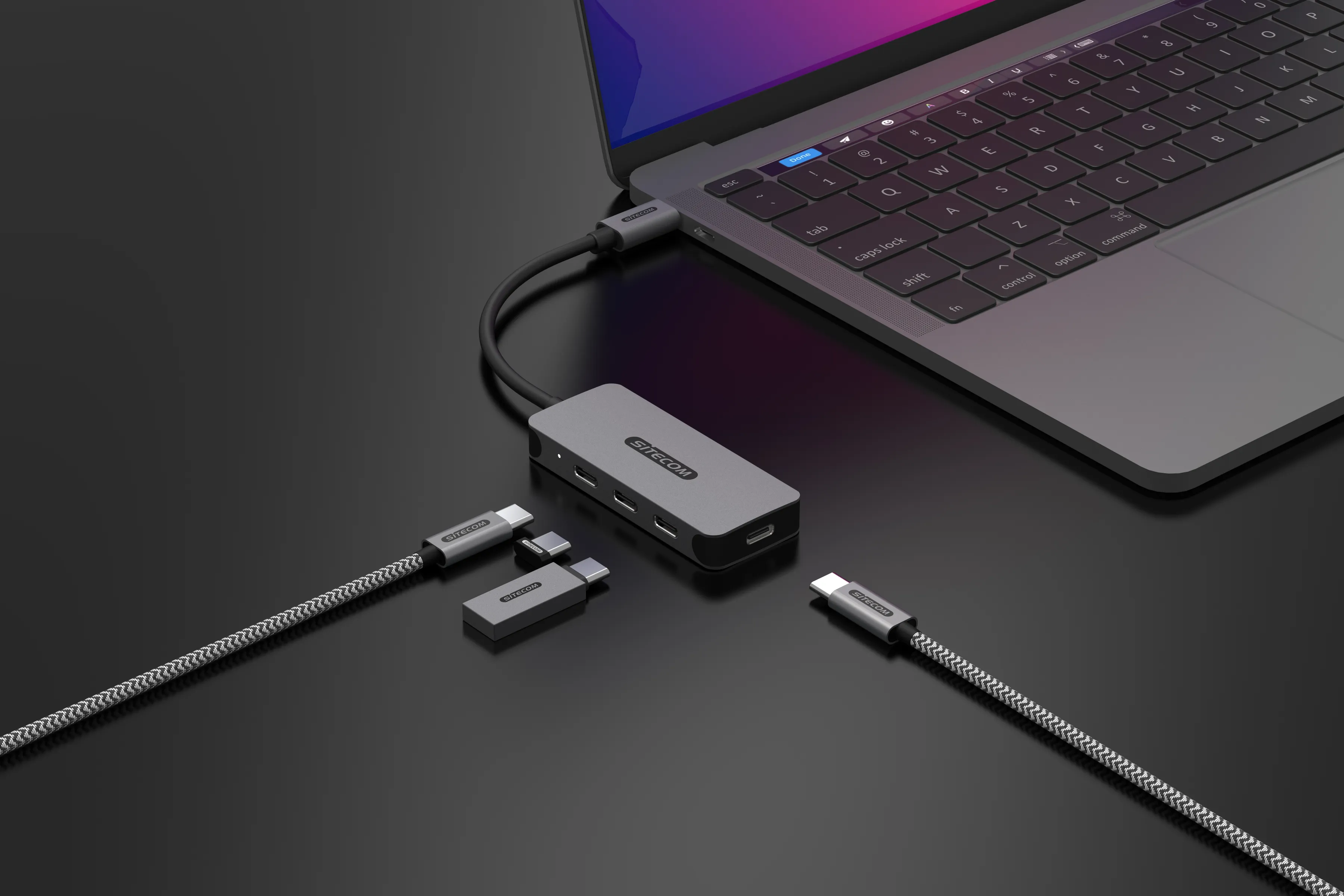 Ein Laptop, der mit einem grauen Hub mit verschiedenen Kabeln und Geräten verbunden ist, vor schwarzem Hintergrund.