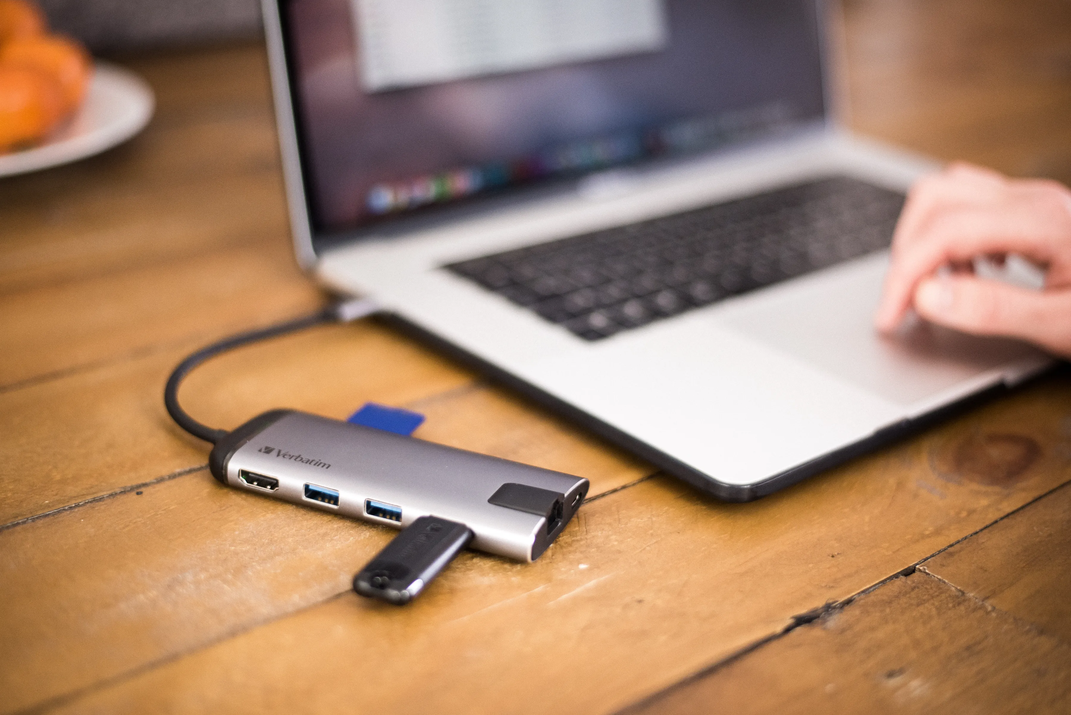Ein Laptop, der mit einem USB-Hub mit einem Flash-Laufwerk und anderen Anschlüssen auf einem Holztisch verbunden ist.