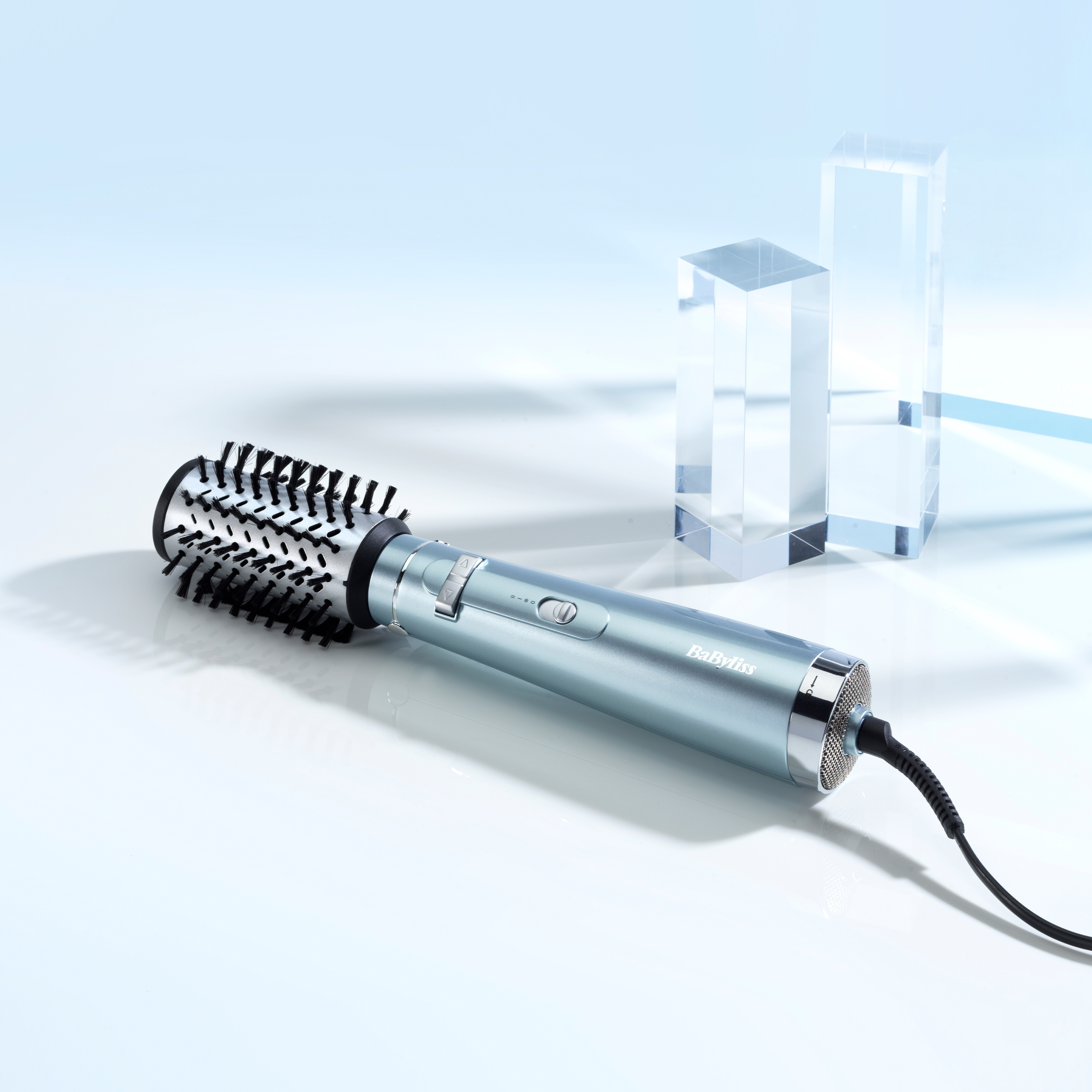 Un moldeador de cabello Babyliss azul claro y dos bloques de acrílico transparente sobre una superficie blanca.