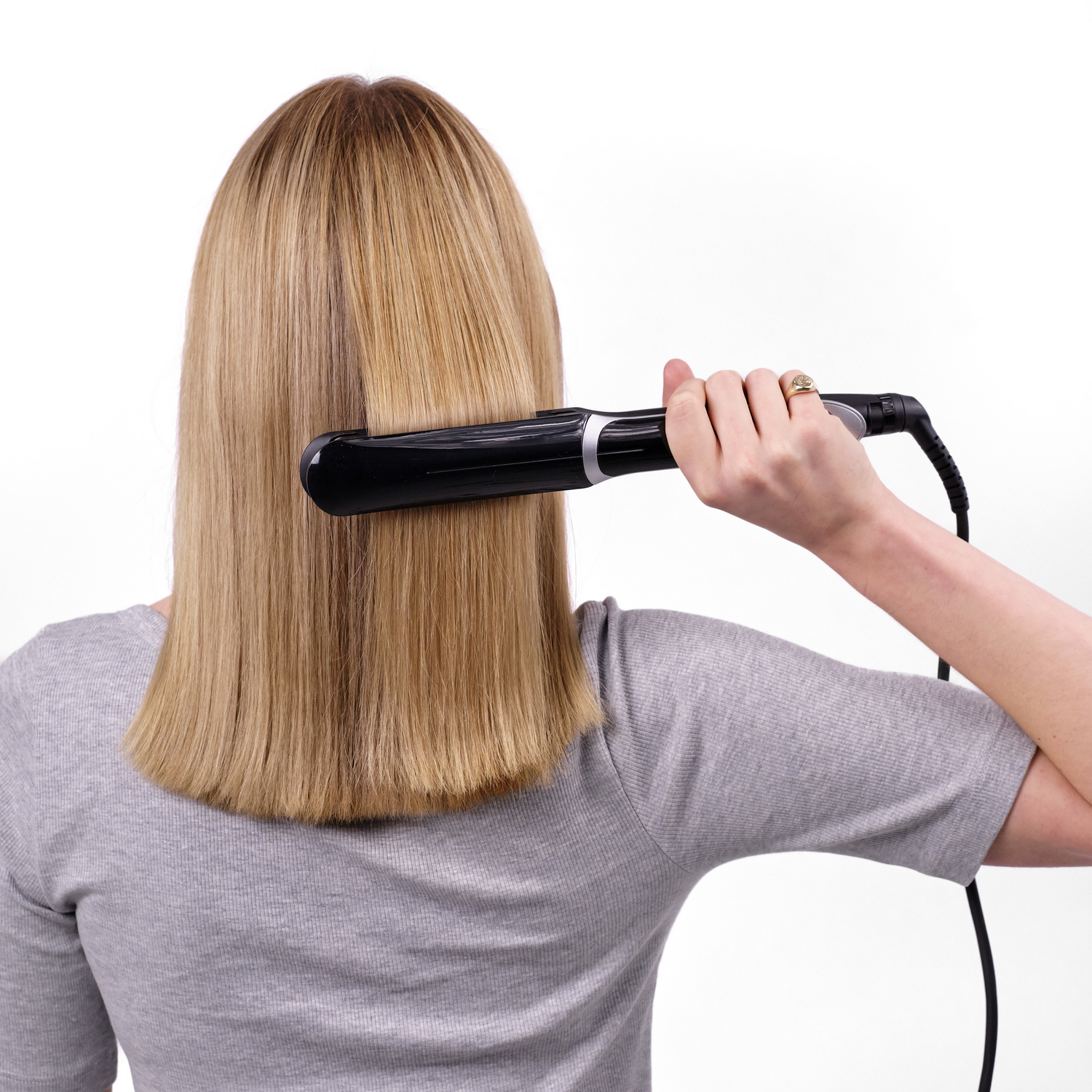 Una mujer se alisa el pelo rubio con una plancha de pelo negra.