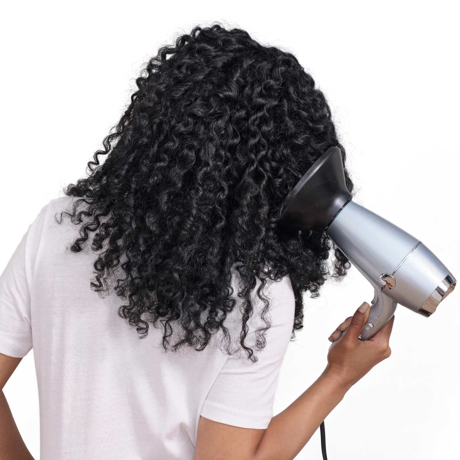 Persona vista de espaldas, secando cabello rizado con secador plateado.