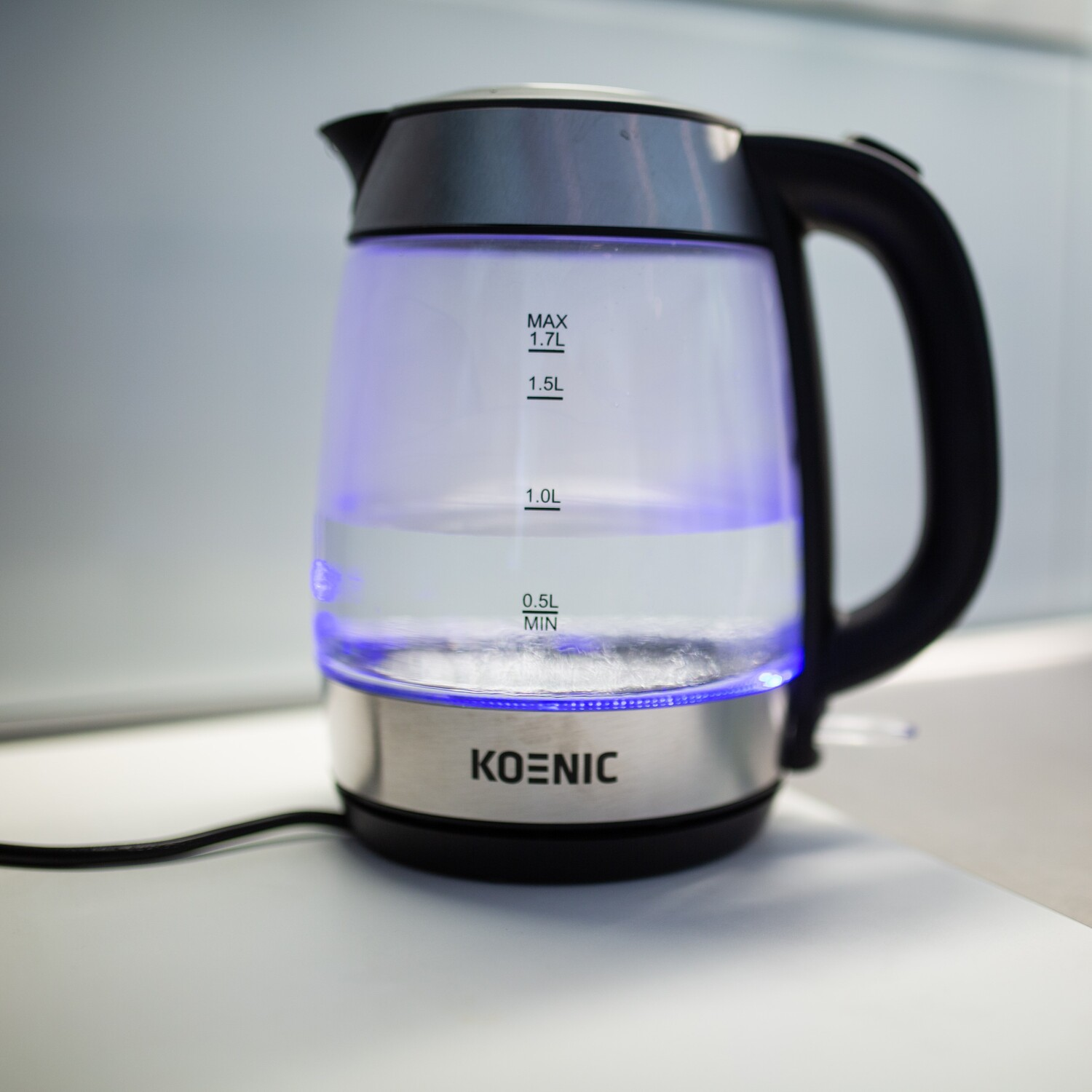 Une bouilloire électrique en verre KOENIC avec une lumière bleue à l'intérieur, indiquant les niveaux d'eau.
