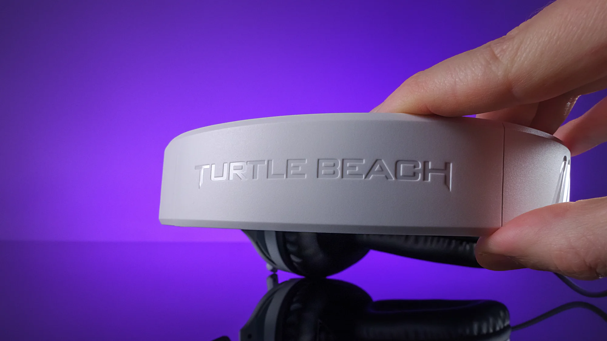 La mano di una persona che tiene la parte superiore di un'auricolare Turtle Beach bianca.