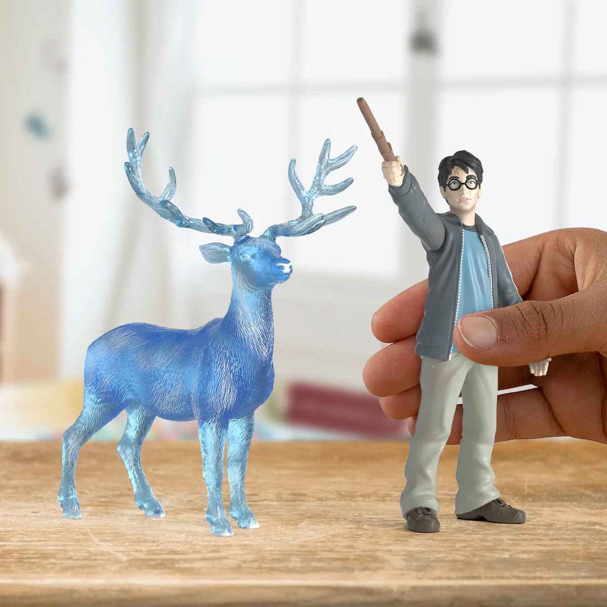 Harry-Potter-Figur mit Zauberstab und Patronus-Hirsch neben sich, auf Holzoberfläche.