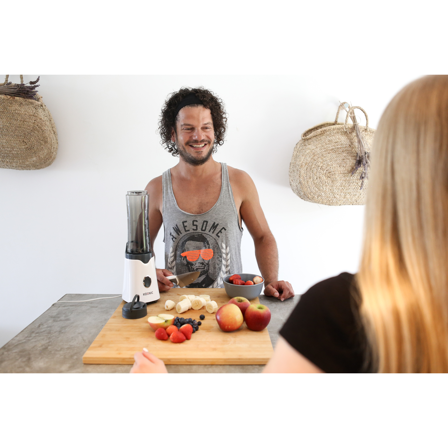 Man making smoothie with a blender. Fruit on a wood board. Woman in the background.
